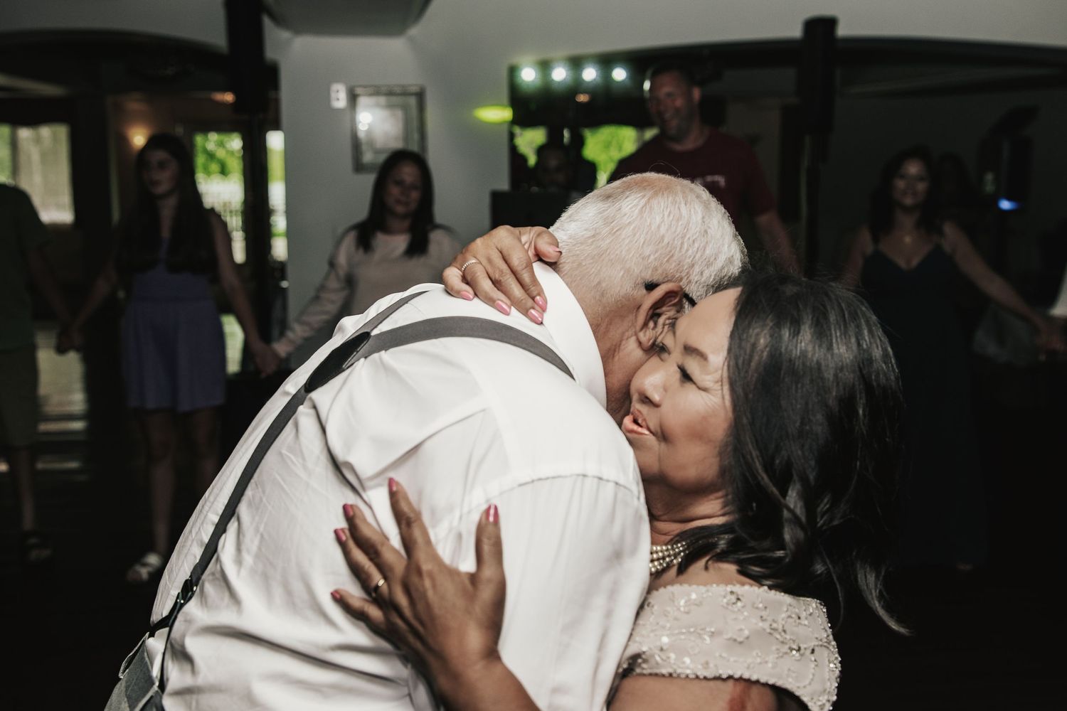 Couple sharing a tender kiss and embrace on the dance floor at a wedding reception with guests in the background.