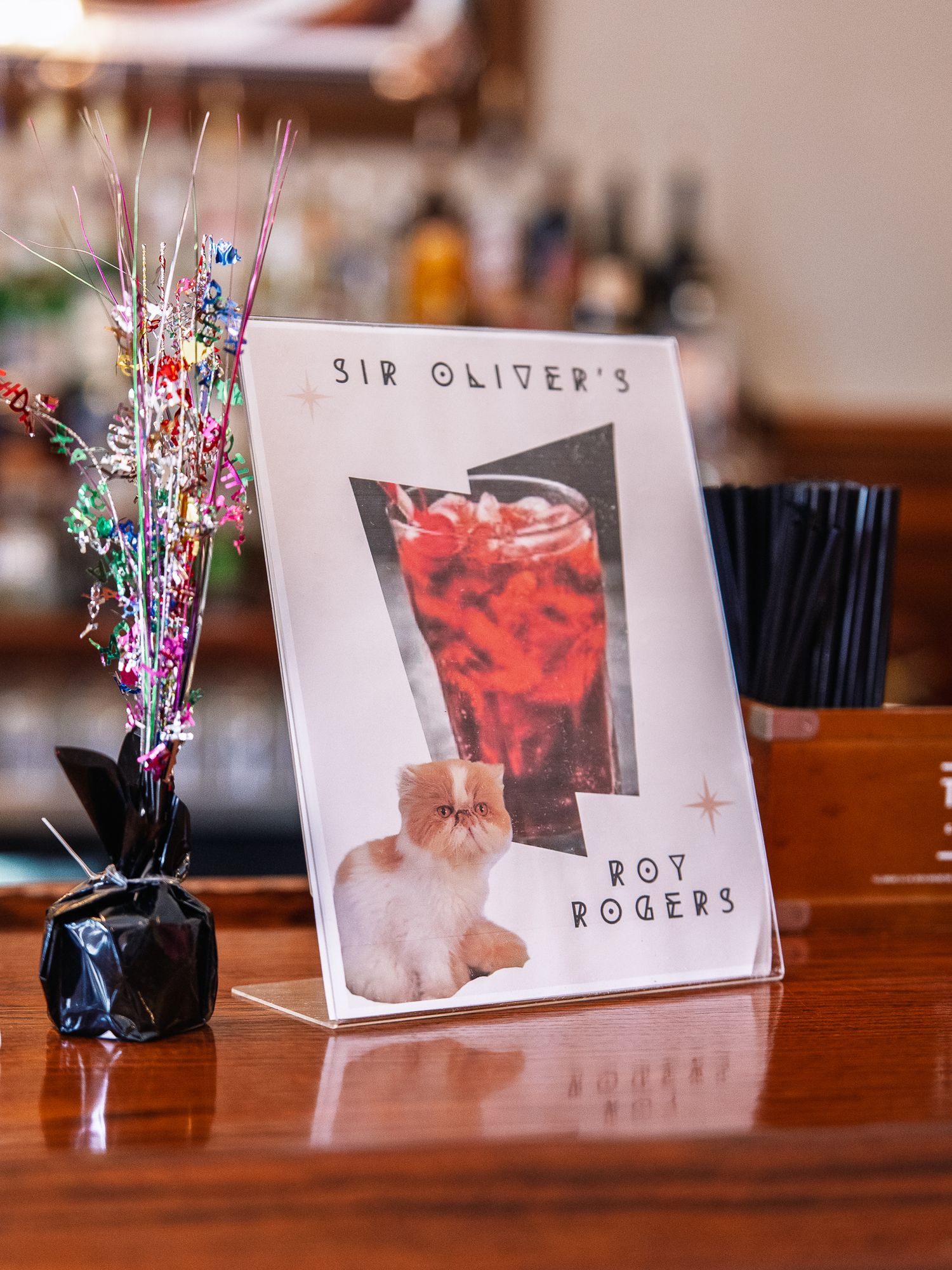Wedding bar menu sign for Sir Oliver's Roy Rogers signature cocktail displayed beside a sparkly floral arrangement.