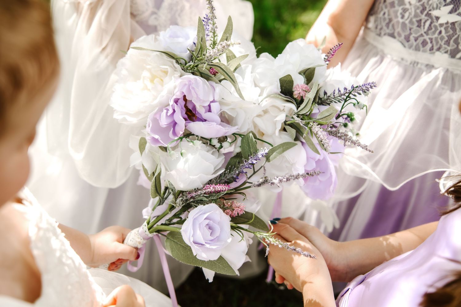 Bridesmaids holding elegant wedding bouquet with white and lavender roses and greenery outdoors.