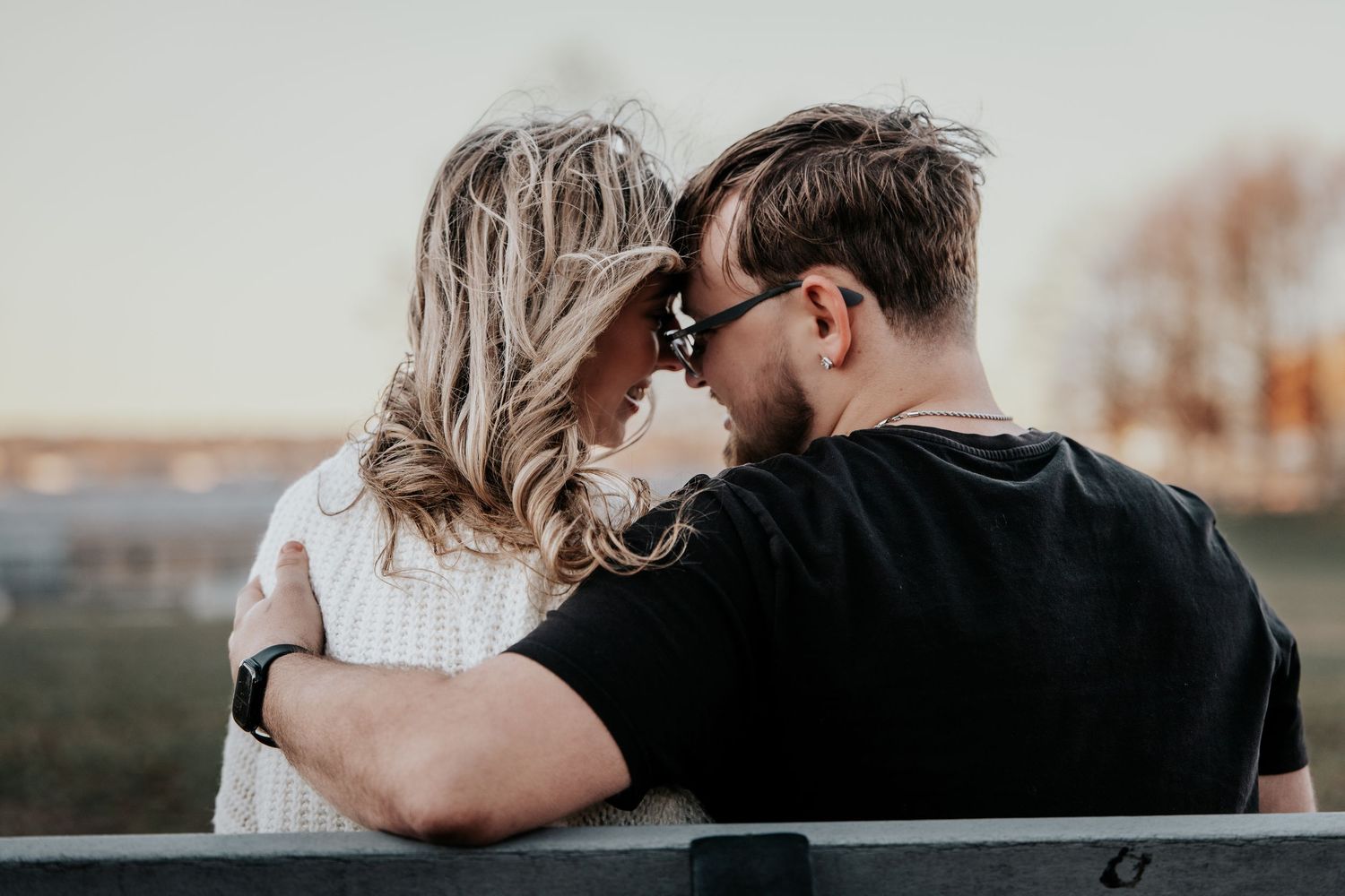 Couple sitting on bench with foreheads touching, woman in white sweater and man in black shirt.
