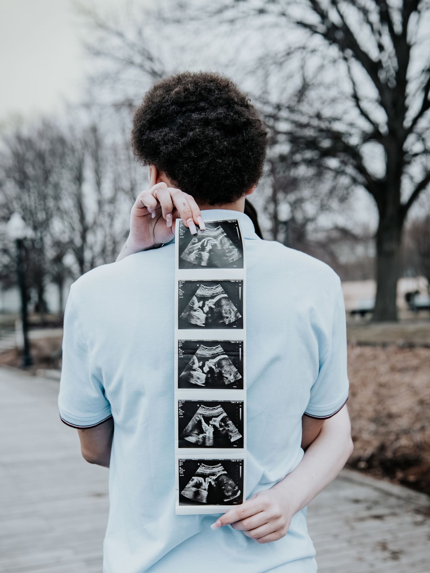 Expectant father holds ultrasound strip behind his back during outdoor maternity photoshoot in winter park.