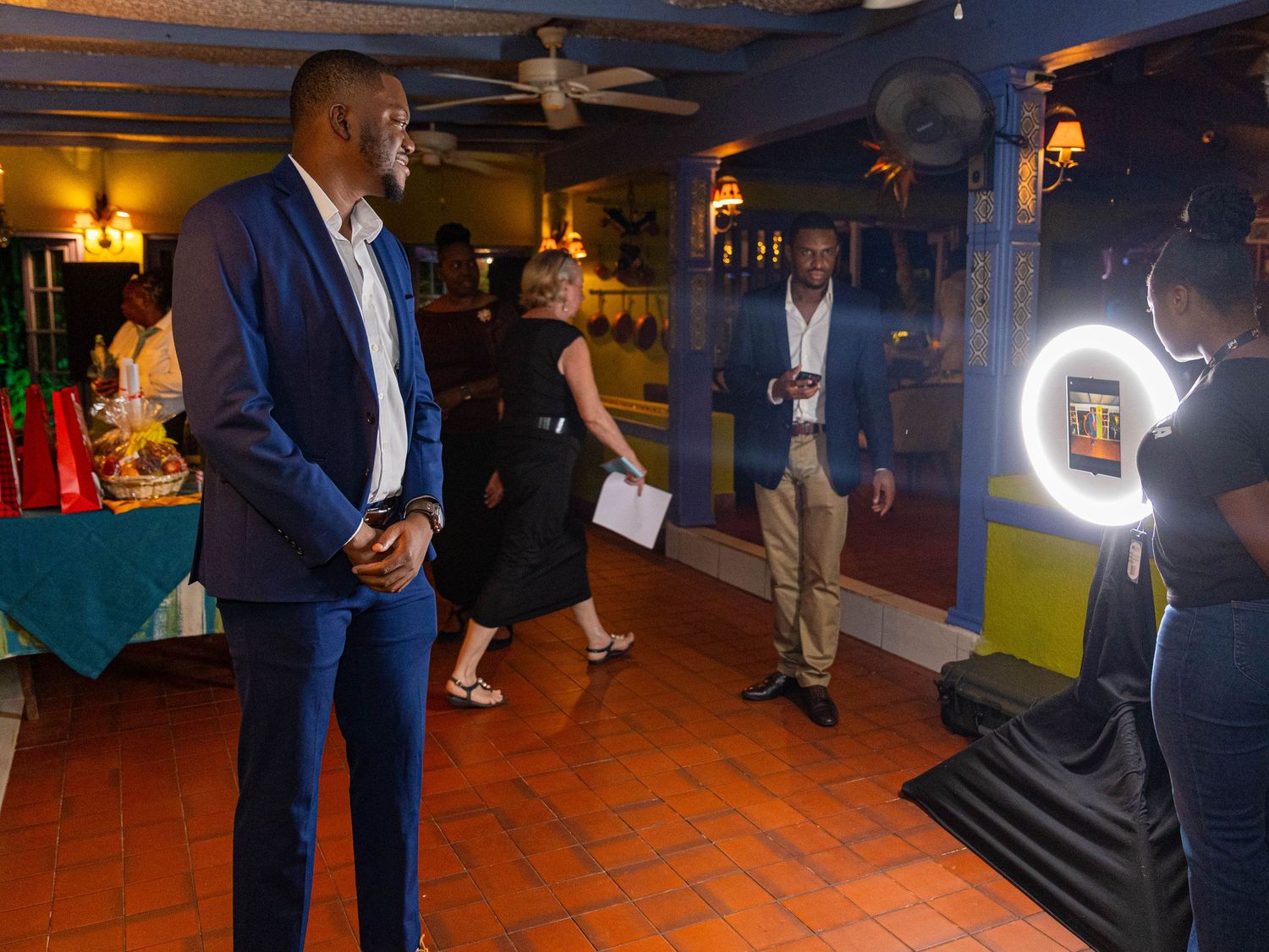 Elegantly dressed guests mingle at an indoor event with ring light, terracotta floors, and vibrant decor.