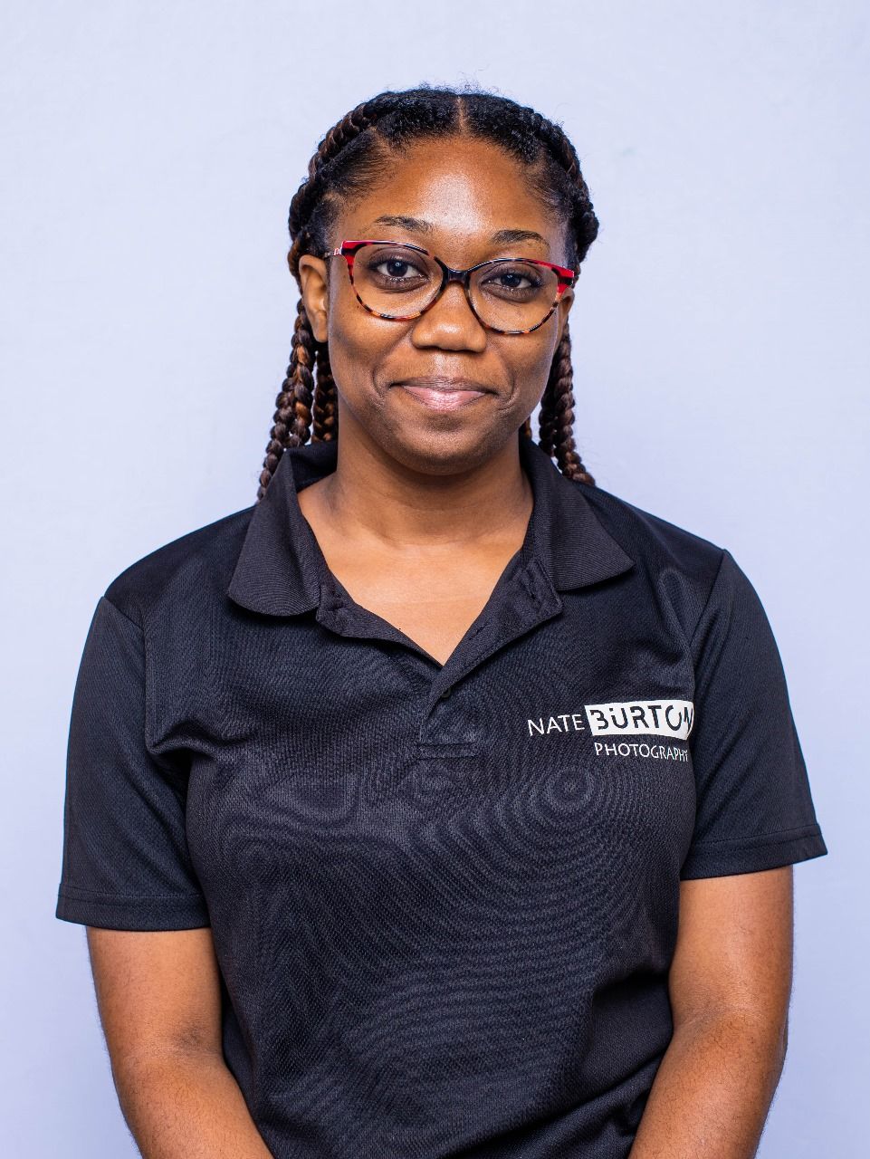 Annique, in red glasses, wearing a black Nate Burton Photography polo shirt, poses for a professional headshot.