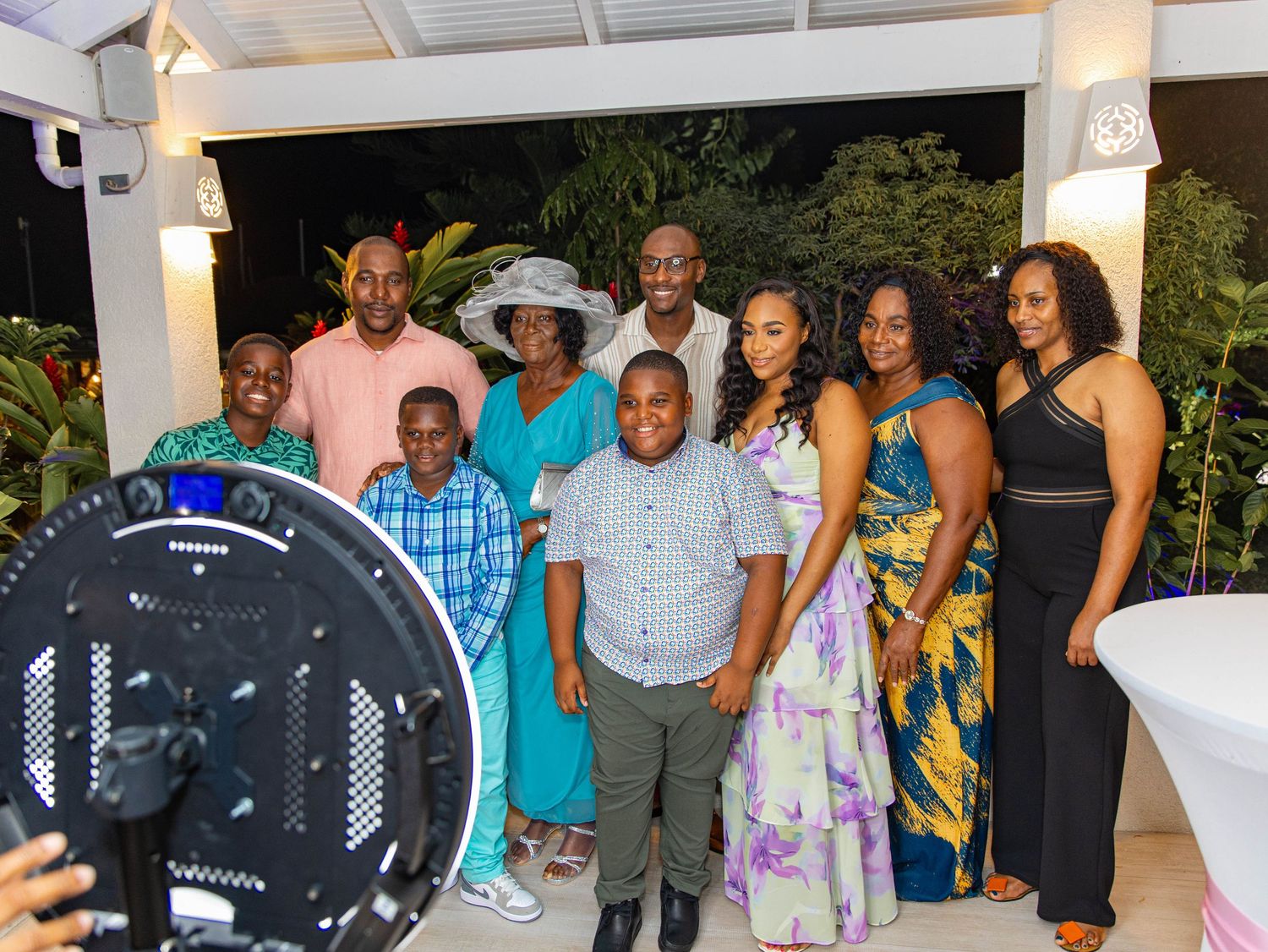 A joyful group of people posing together at an outdoor evening celebration, dressed in colorful formal attire.