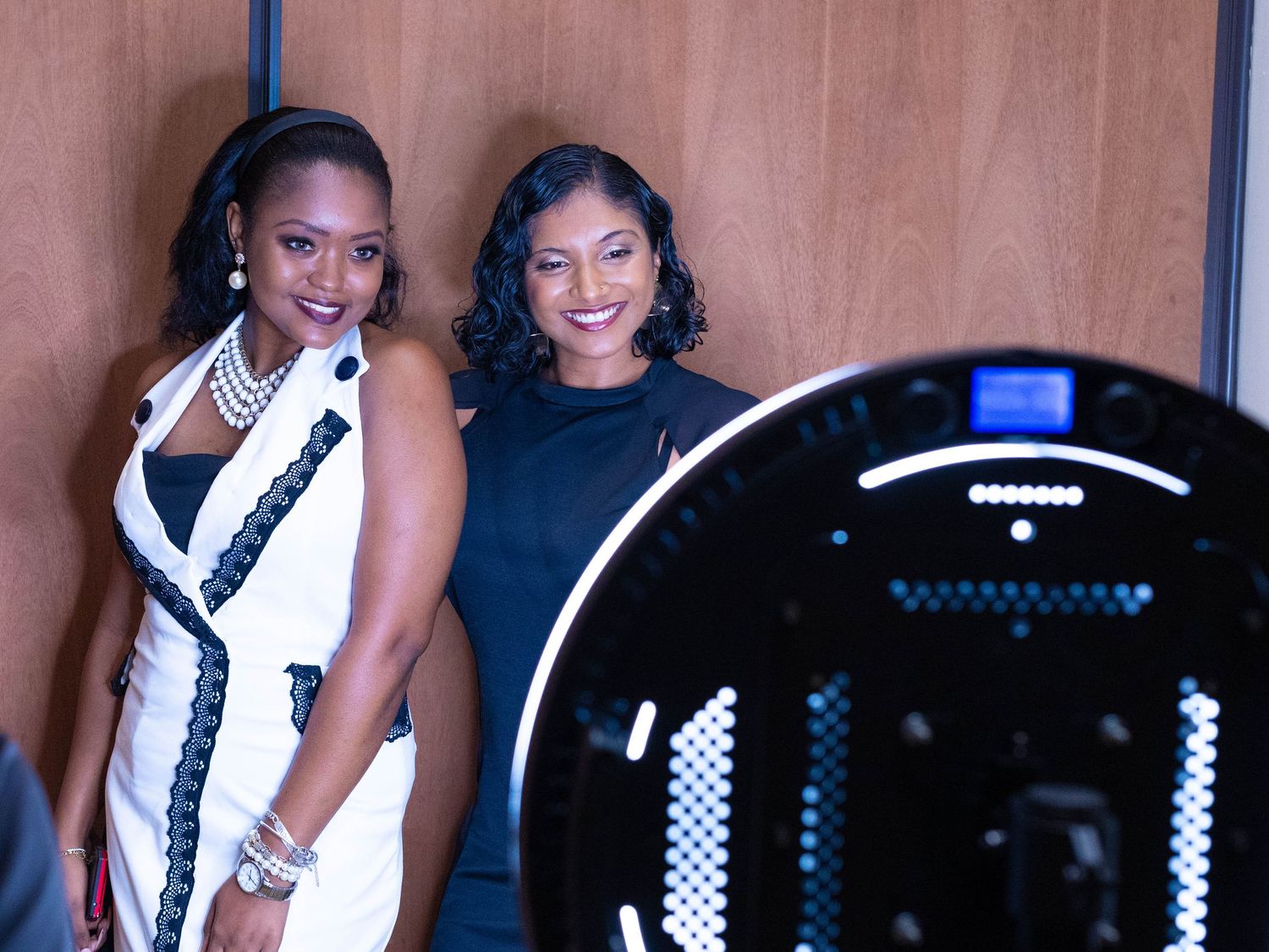 Two women smiling together near a ring light at a professional photo booth event.