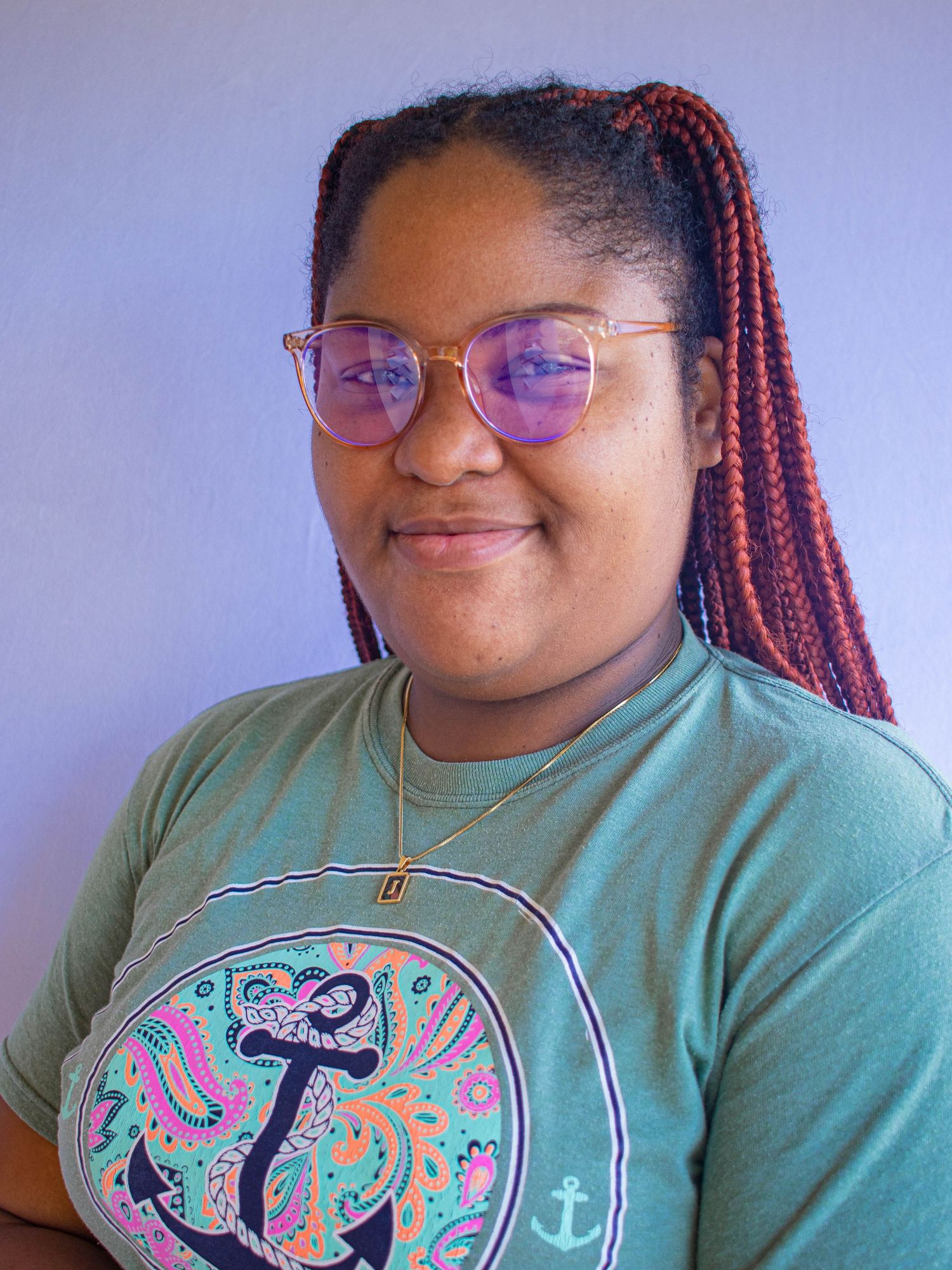 Jaleesa with red braids and glasses wearing a teal anchor graphic T-shirt, smiling against a background.