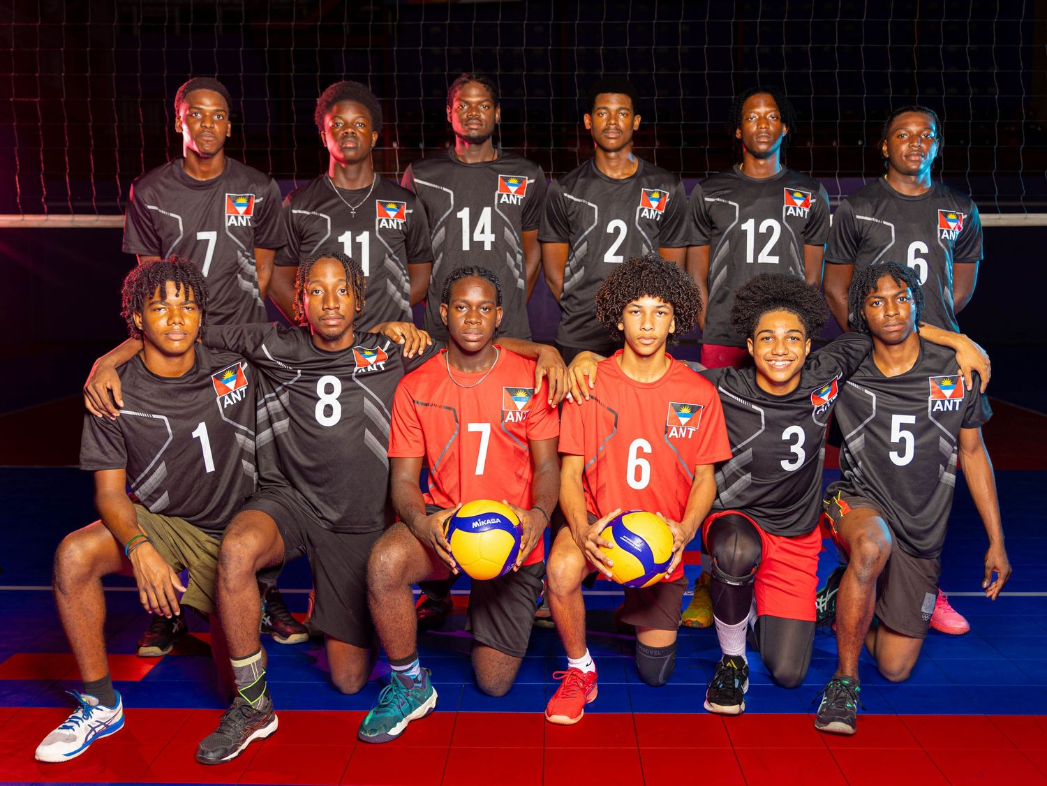 Youth volleyball team poses for a group photo in black and red uniforms, holding Mikasa volleyballs.