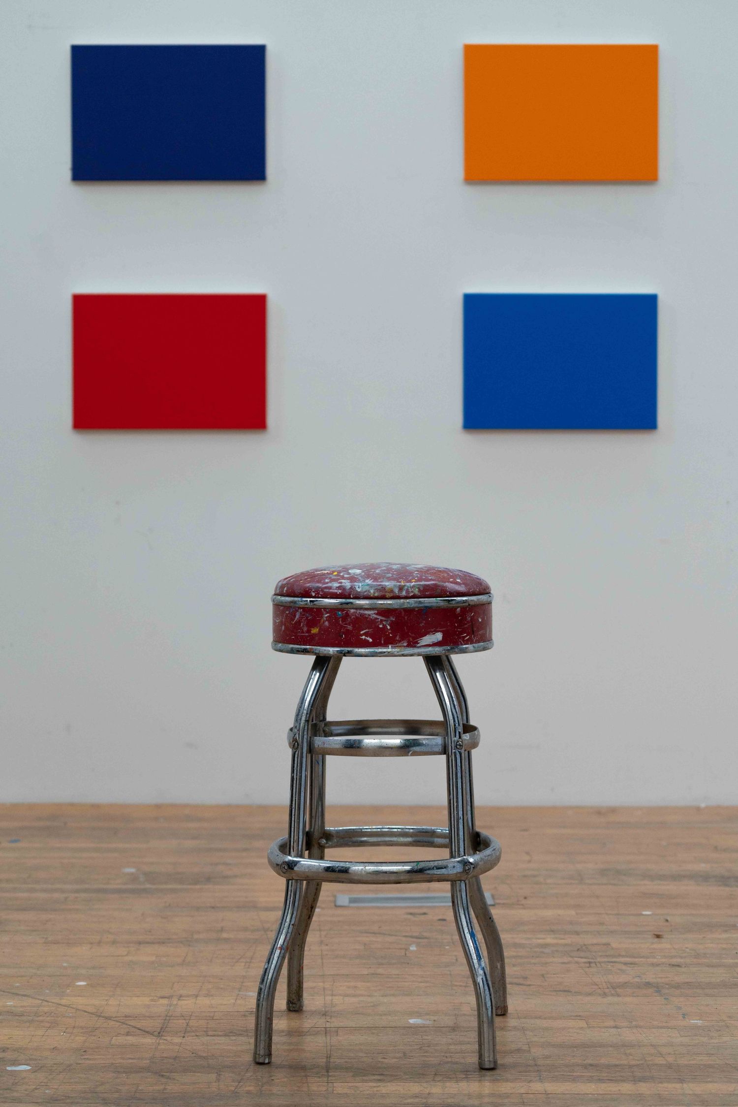 Vintage red chrome bar stool in front of four colorful rectangular canvas paintings.