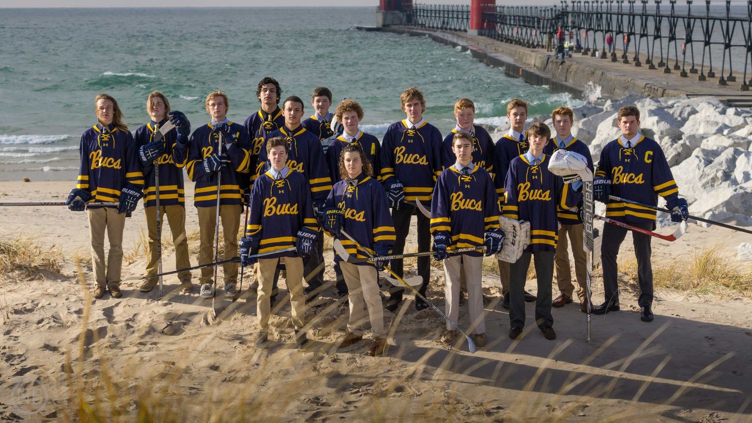 Youth hockey team in blue jerseys posing on beach near pier.
