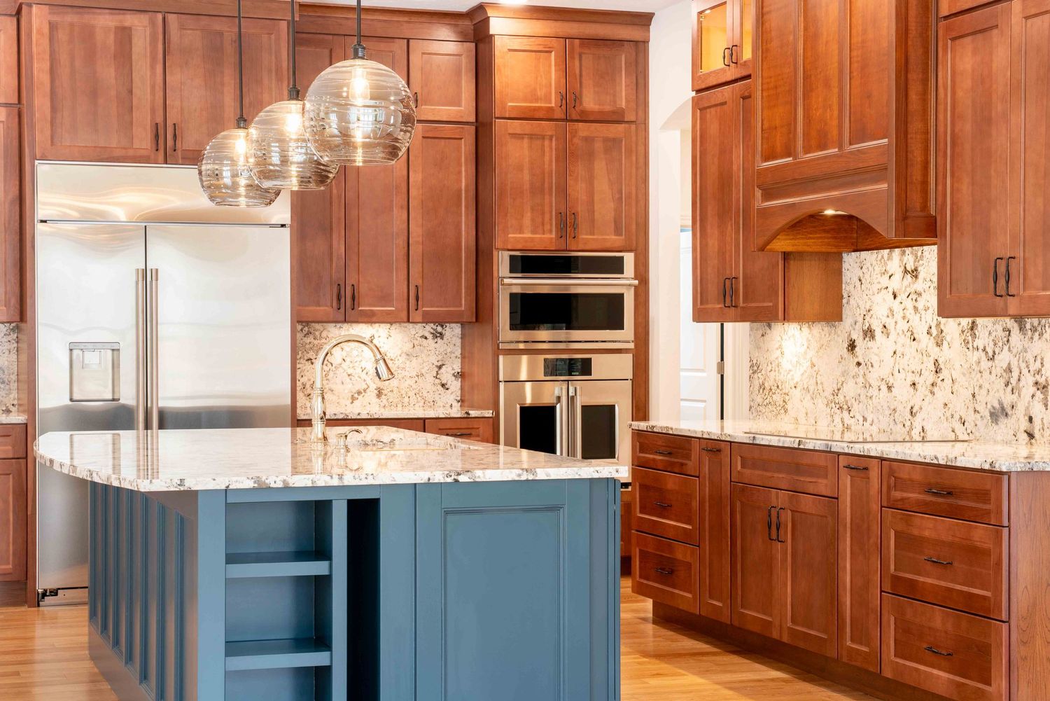 Luxury kitchen with warm cherry wood cabinets, blue island, marble backsplash, and pendant lights.