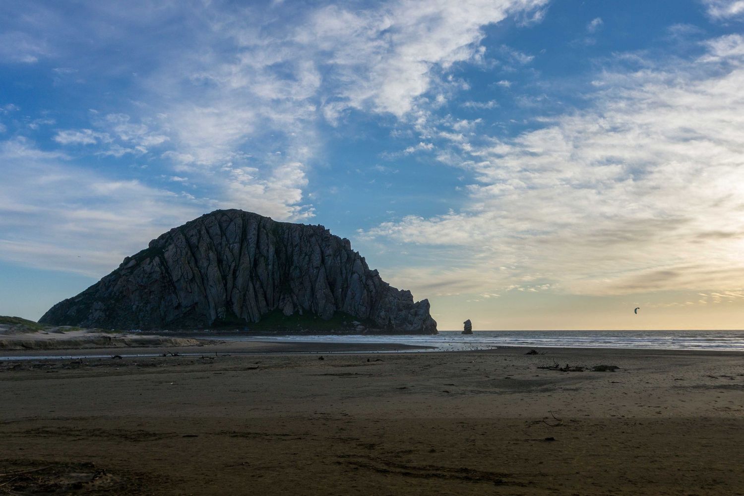 Morro Rock rises dramatically above a sandy beach under a partly cloudy sky at golden hour.