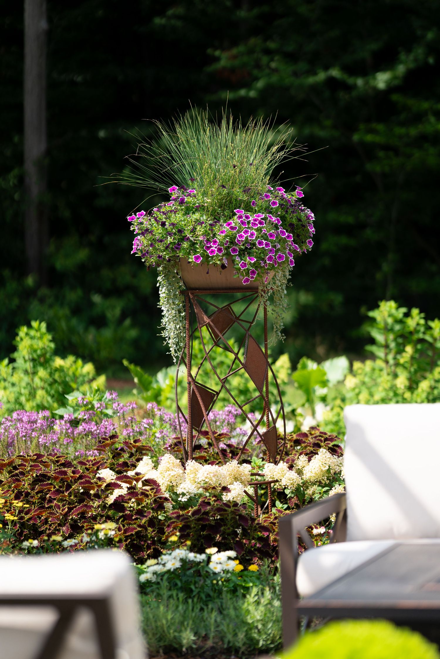 Decorative elevated planter with purple petunias and ornamental grass on garden patio.