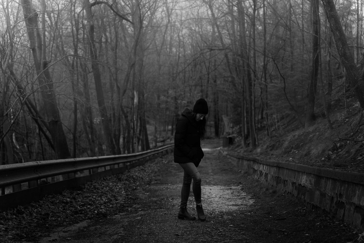 Black and white photo of lone figure walking on misty forest road.