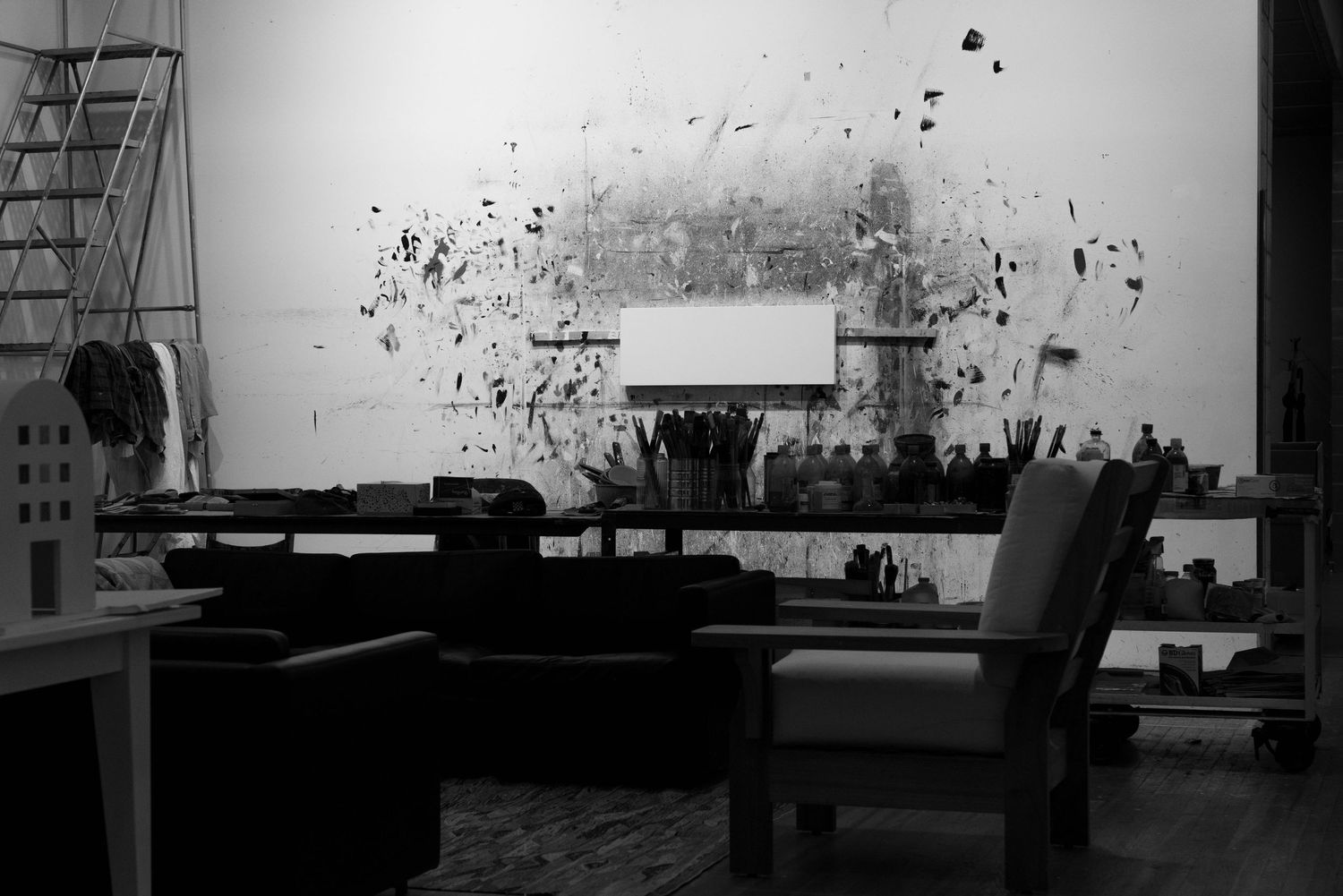 Black and white artist studio interior with ink splatter artwork on wall and art supplies on desk.
