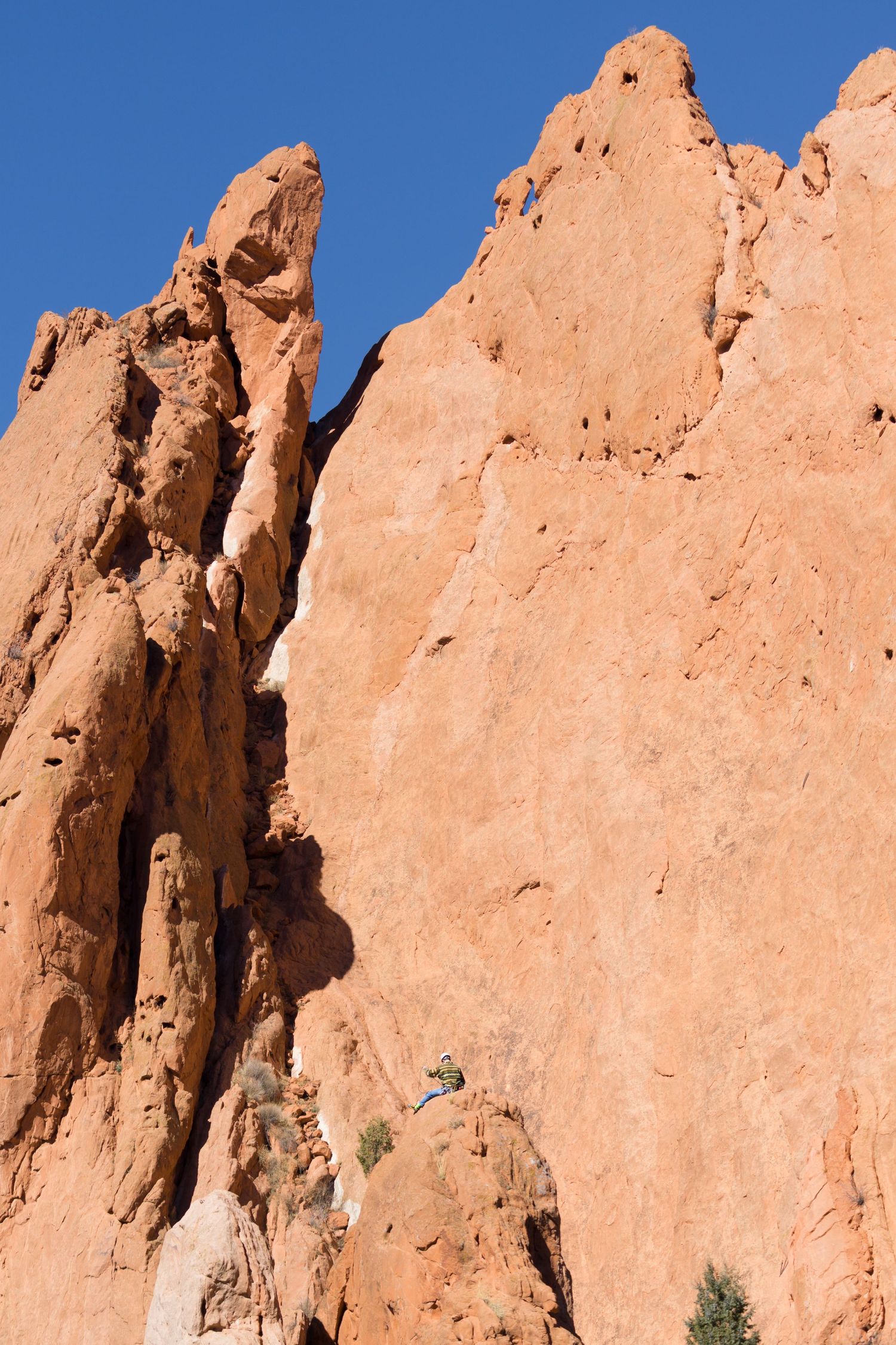 Climber scales towering red sandstone rock formations under a vivid blue sky.