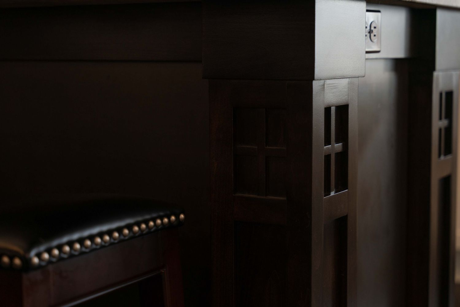 Dark wood craftsman-style cabinet detail with decorative grid panels in dim lighting.