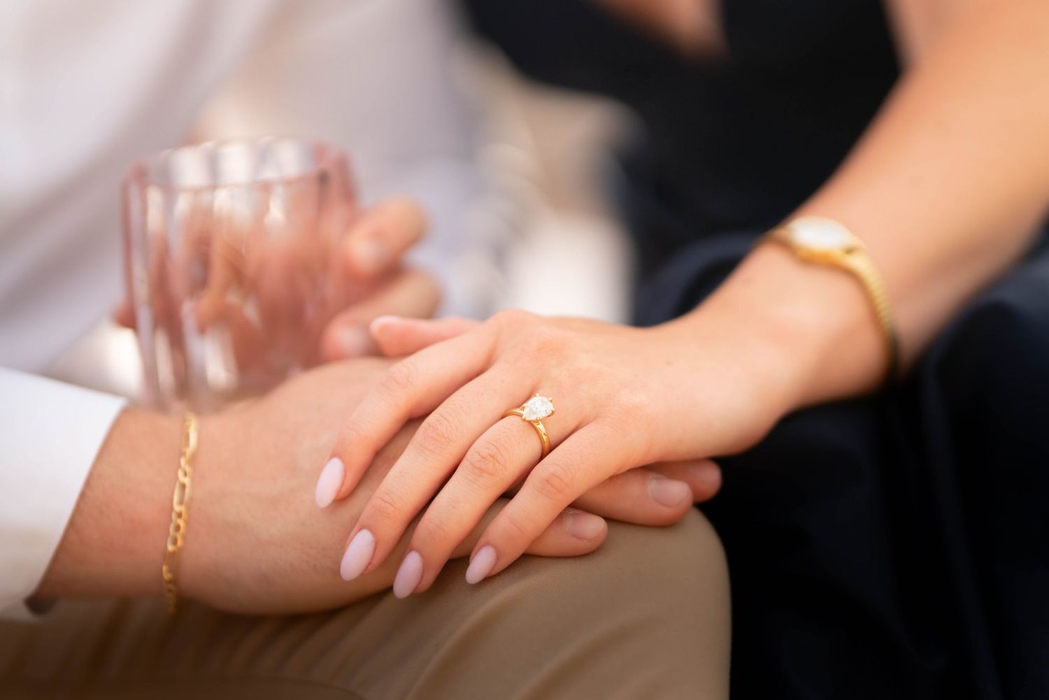 Close-up of a woman's hand with an engagement ring resting on a man's hand outdoors.