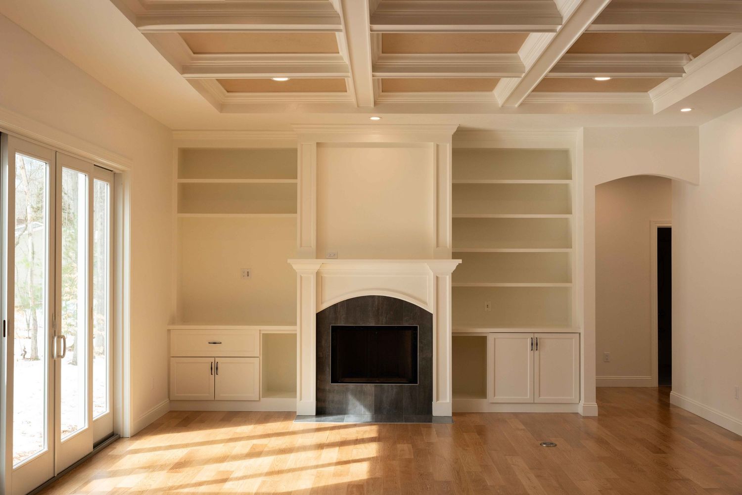 Bright living room with coffered ceiling, white fireplace, built-in shelves, and hardwood floors.