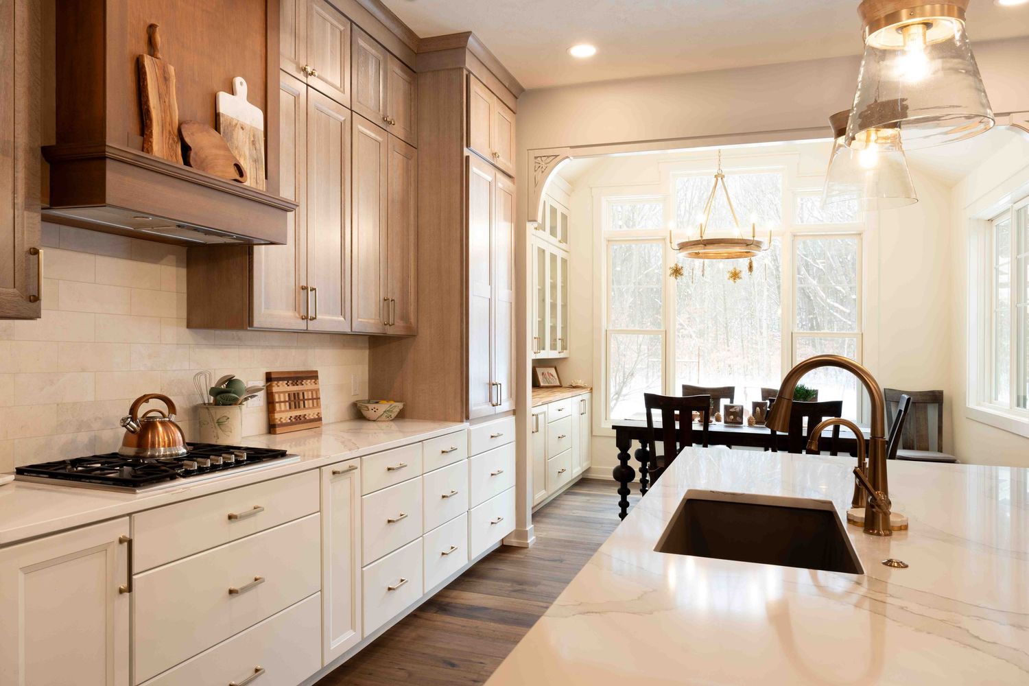 Modern kitchen with two-tone cabinets, quartz island, bronze faucet, and breakfast nook beyond arch.