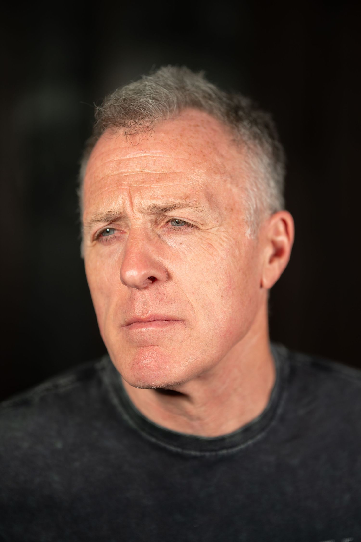 Close-up portrait of a serious middle-aged man with gray hair against a dark background.