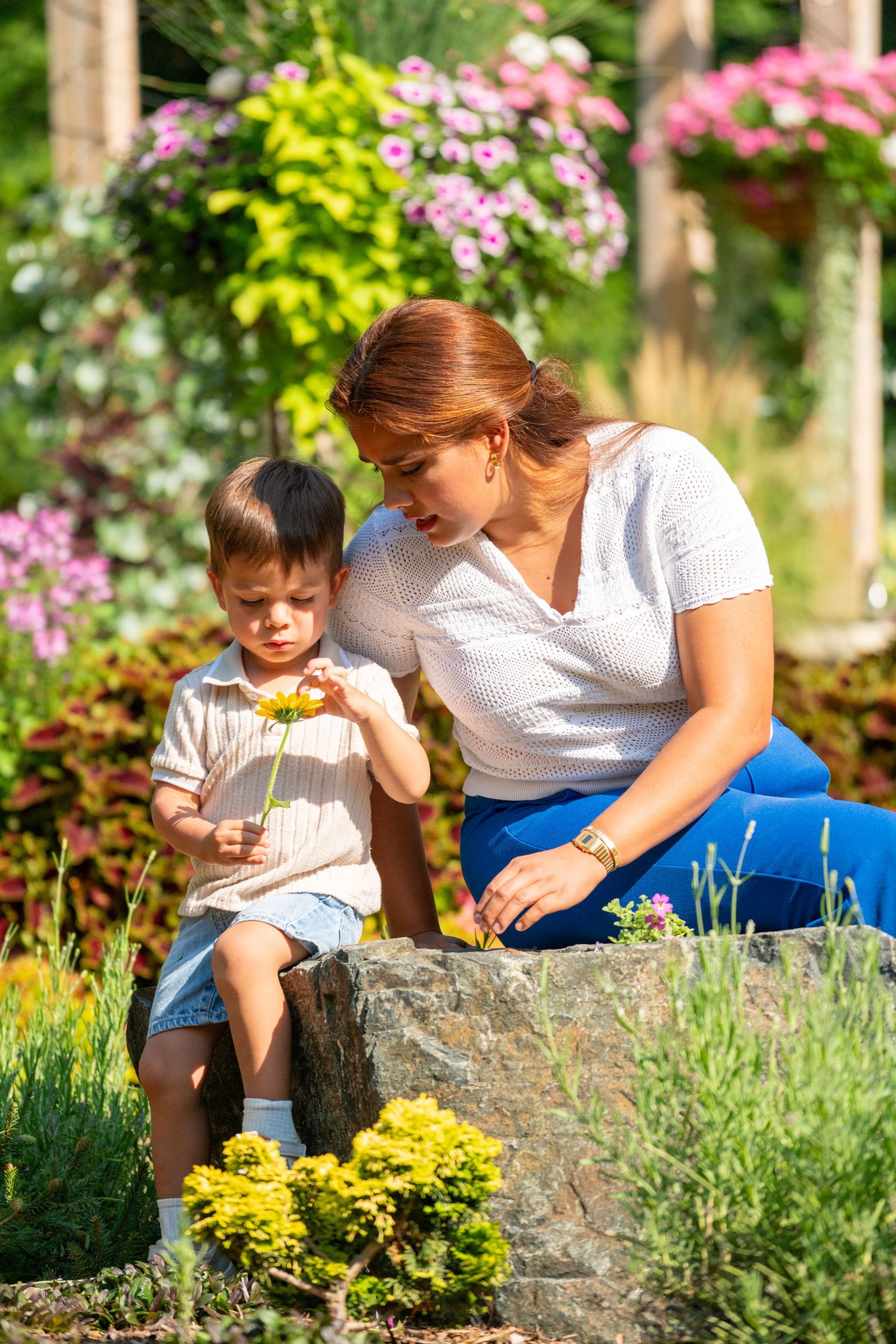 Mother and young child examining flowers together in a sunny colorful garden.