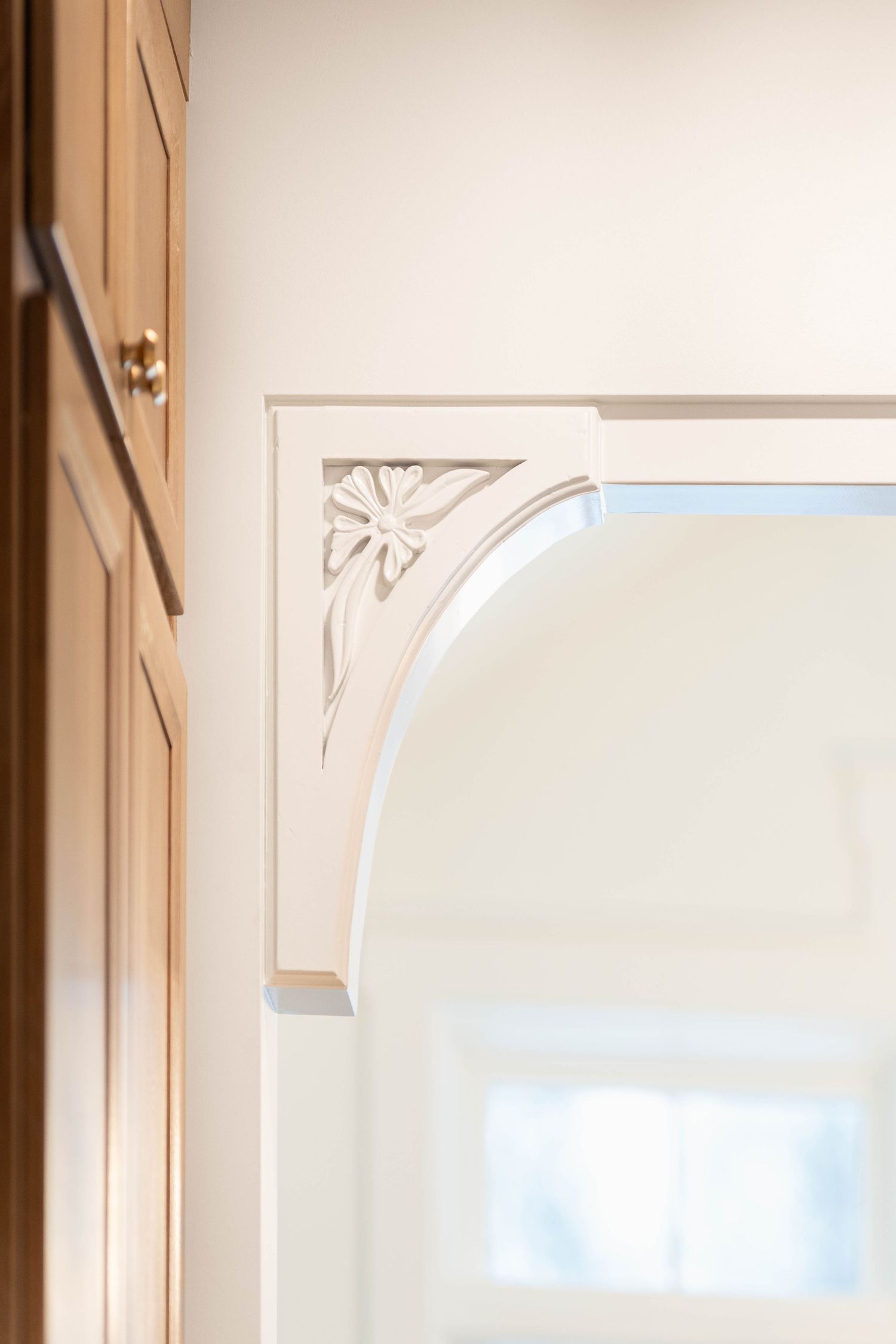 Ornate white carved corbel bracket with floral motif framing an arched glass cabinet doorway.