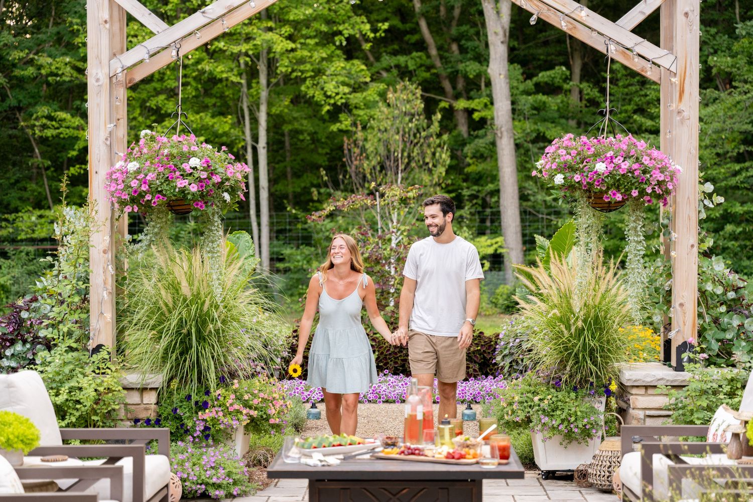 Happy couple holding hands in a lush garden patio with hanging flower baskets.