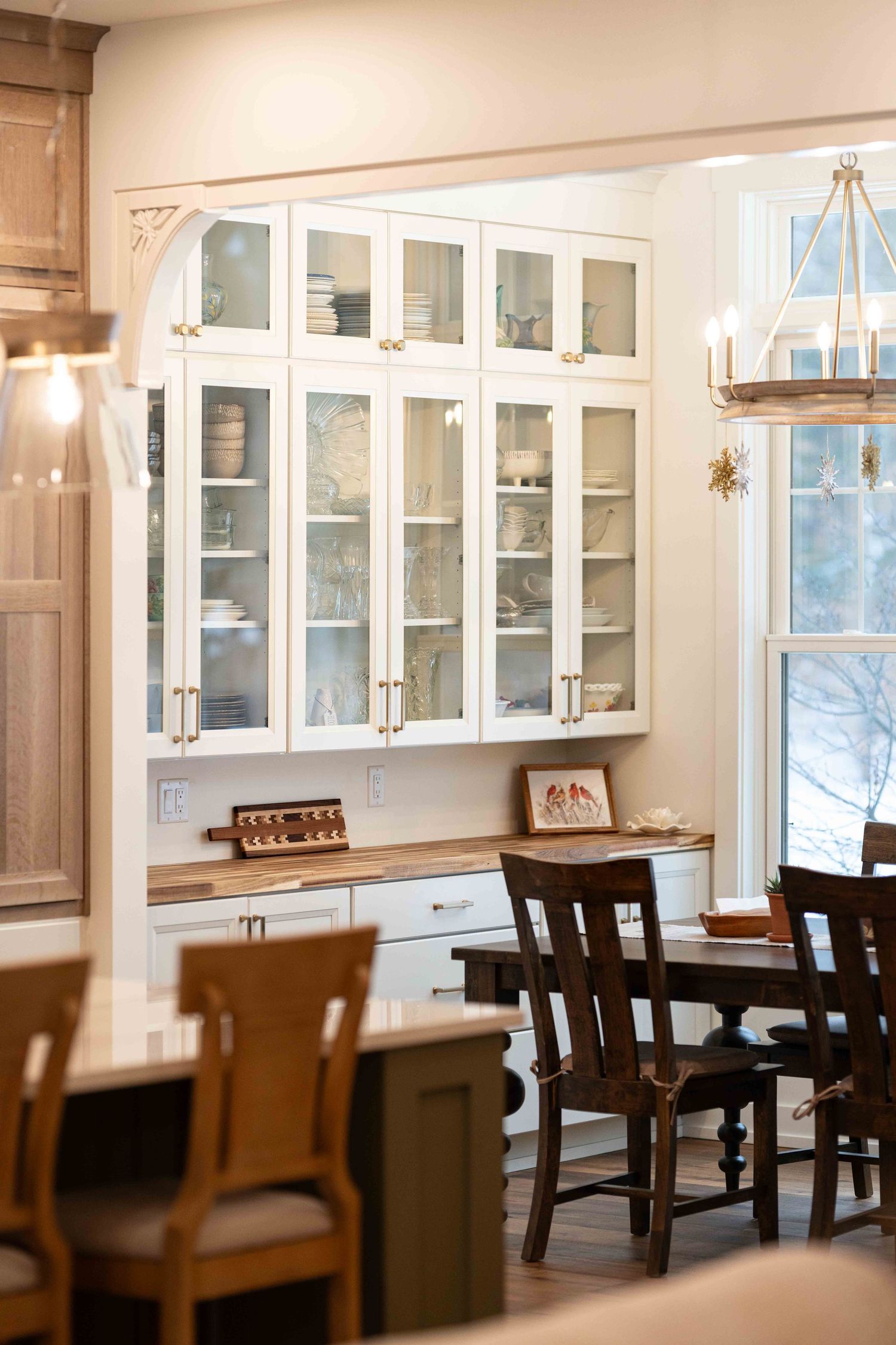 Elegant dining room with white glass-front cabinets, wood table, dark chairs, and brass chandelier.