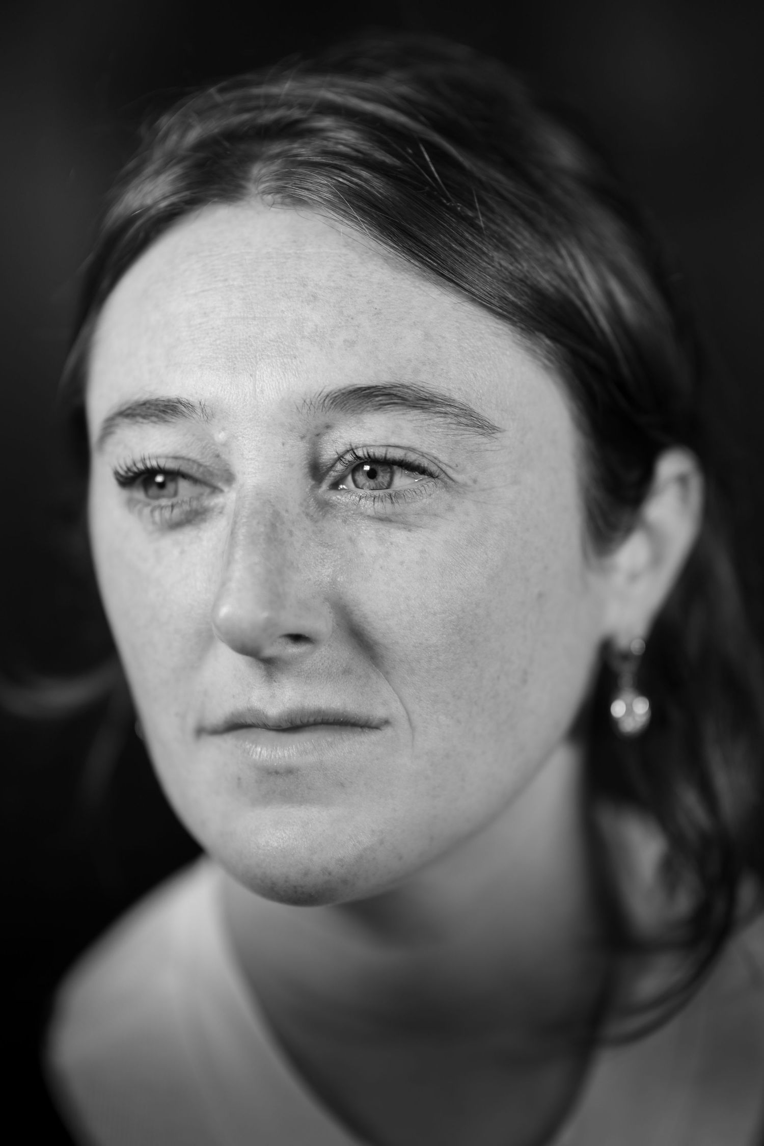 Black and white close-up portrait of a woman with freckles and earrings.