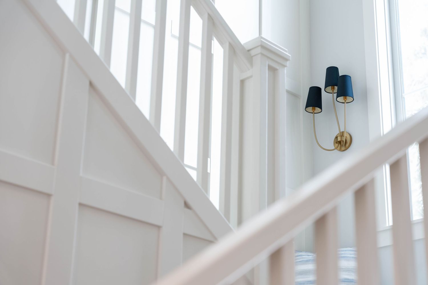 White staircase with elegant brass wall sconce featuring navy blue shades in a bright modern home.