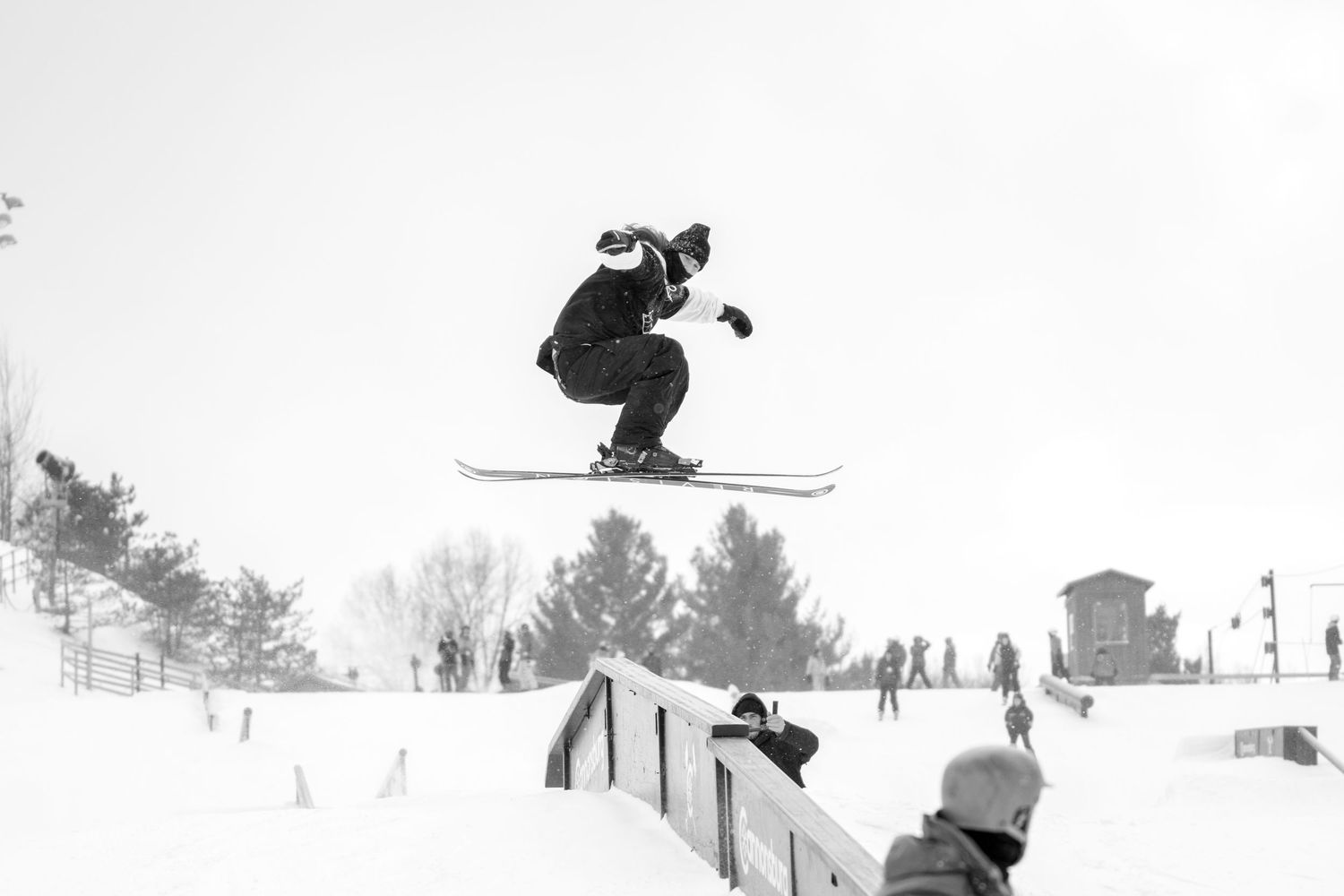 Snowboarder performs aerial trick over a rail jump at a snow park in winter.