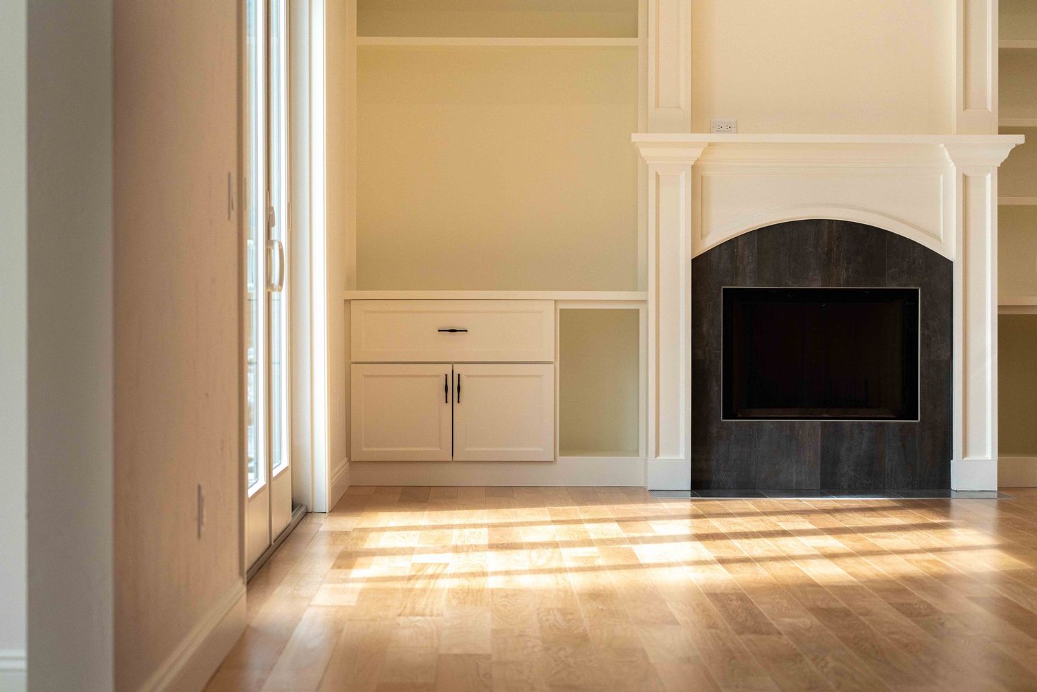 Elegant living room with white built-in cabinets, arched black fireplace surround, and hardwood floors.