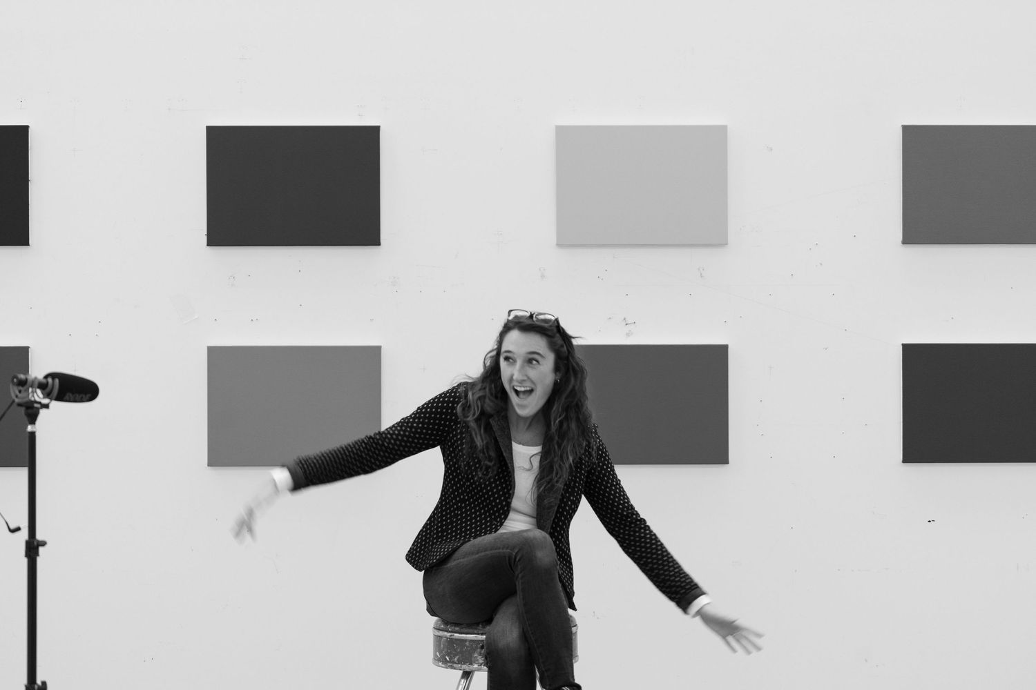Excited woman posing in front of gray color block paintings on white gallery wall.