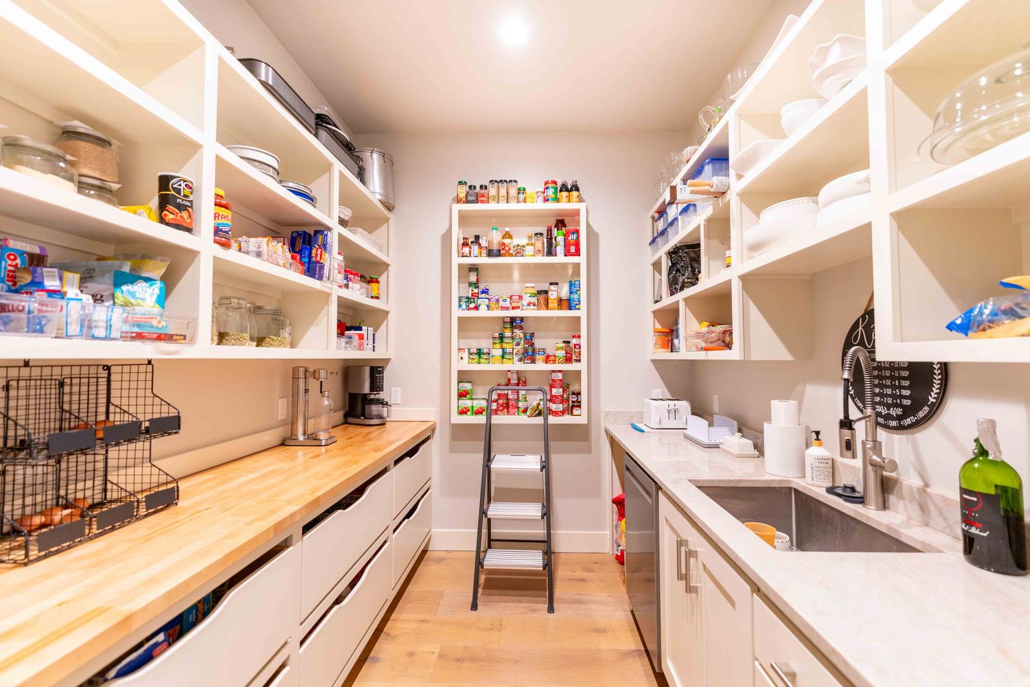 Large walk-in pantry with open white shelving, butcher block counter, and utility sink.