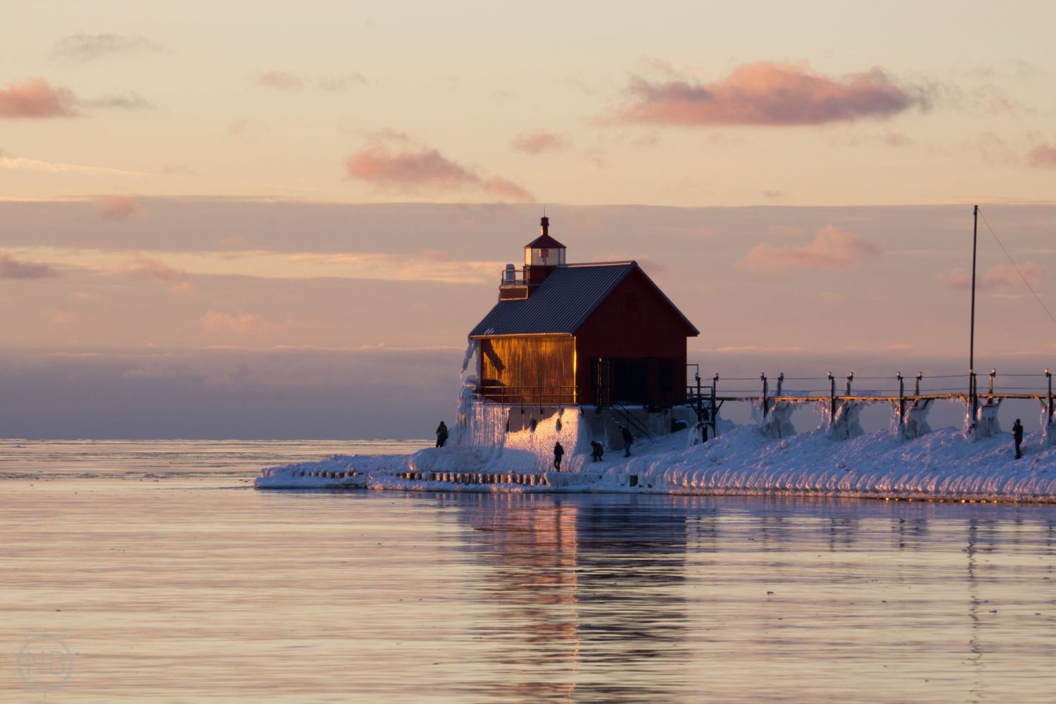 Snow-covered lighthouse glowing warmly at sunset on a frozen Lake Michigan pier in winter.