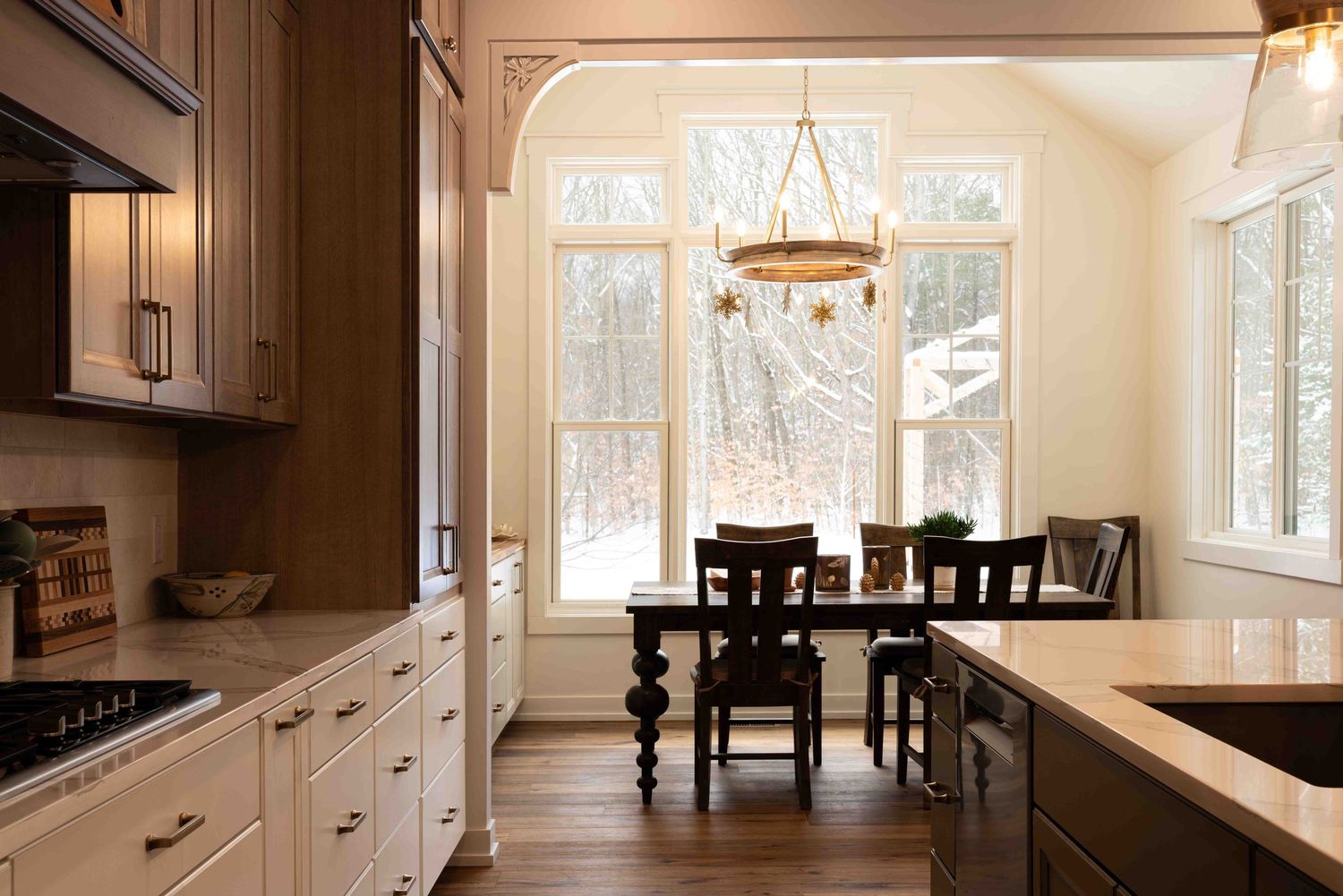Cozy kitchen dining nook with dark wood cabinets, arched windows, and rustic chandelier.