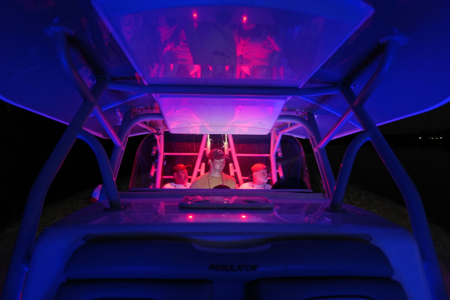 Interior of a boat glowing with blue and red neon lights at night on the water.
