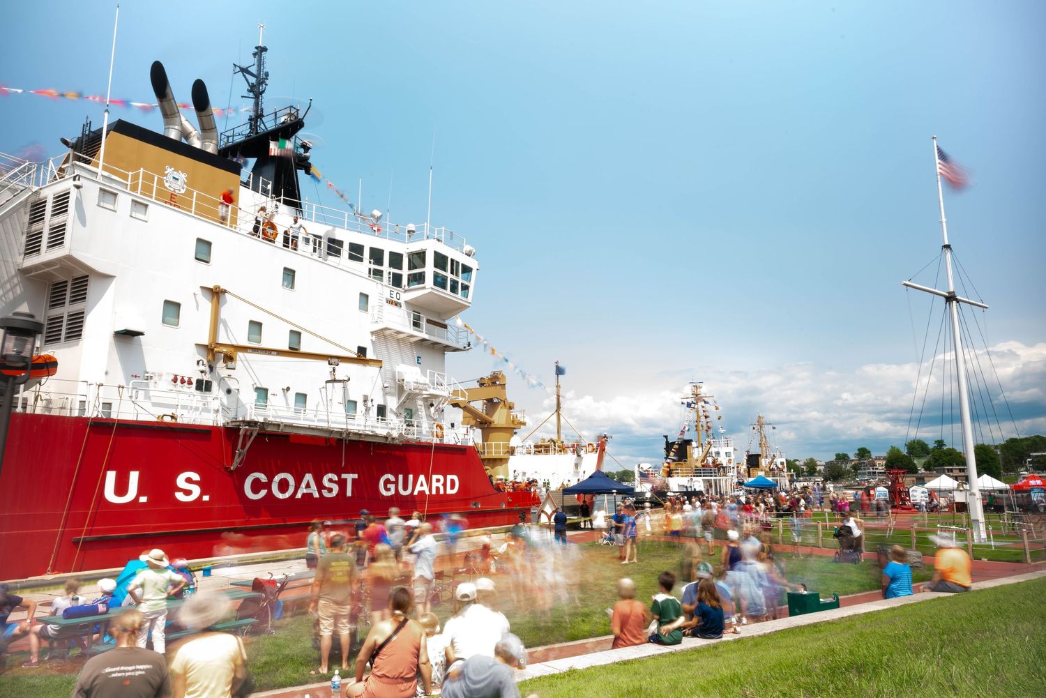 US Coast Guard ship docked at a public event with crowds gathered on a sunny day.