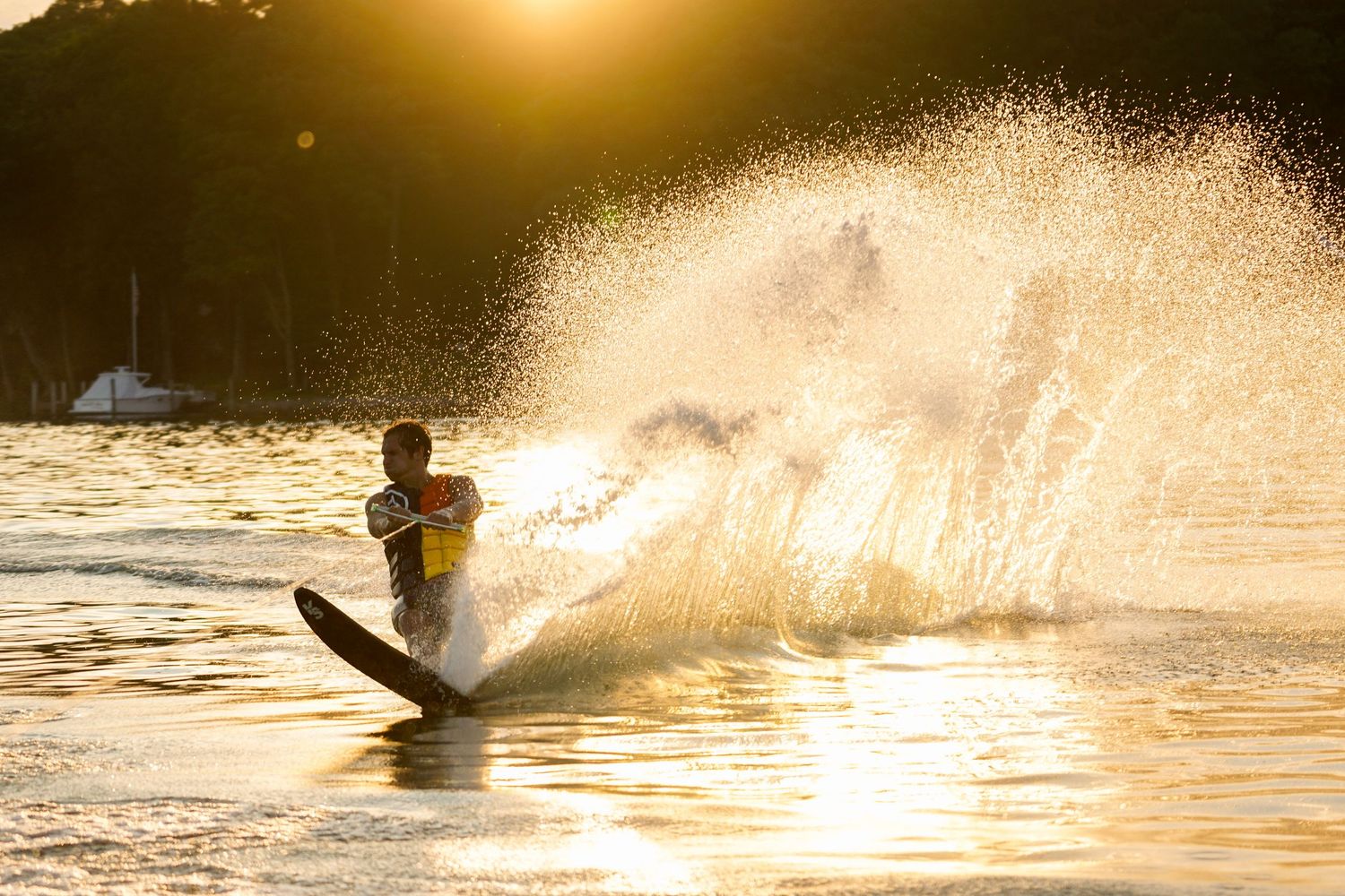 Silhouette of a water skier creating dramatic spray on a lake during golden sunset light.