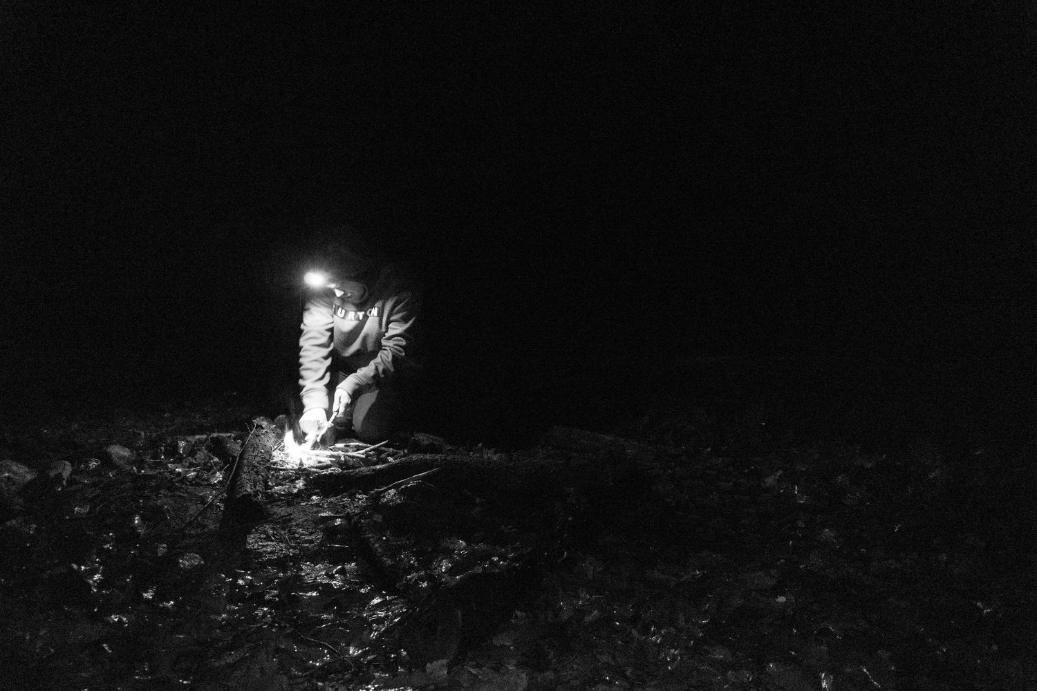 Person working by lantern light in a dark outdoor night scene in black and white.