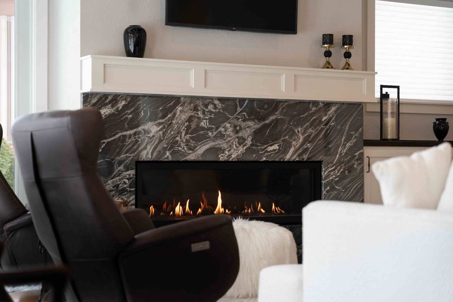 Linear gas fireplace with dramatic gray marble surround and brown leather recliner chair.