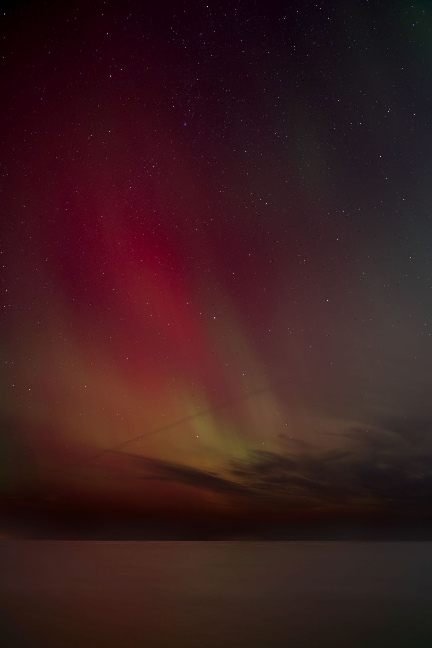 Vibrant red and green aurora borealis northern lights dancing over a calm reflective lake at night.