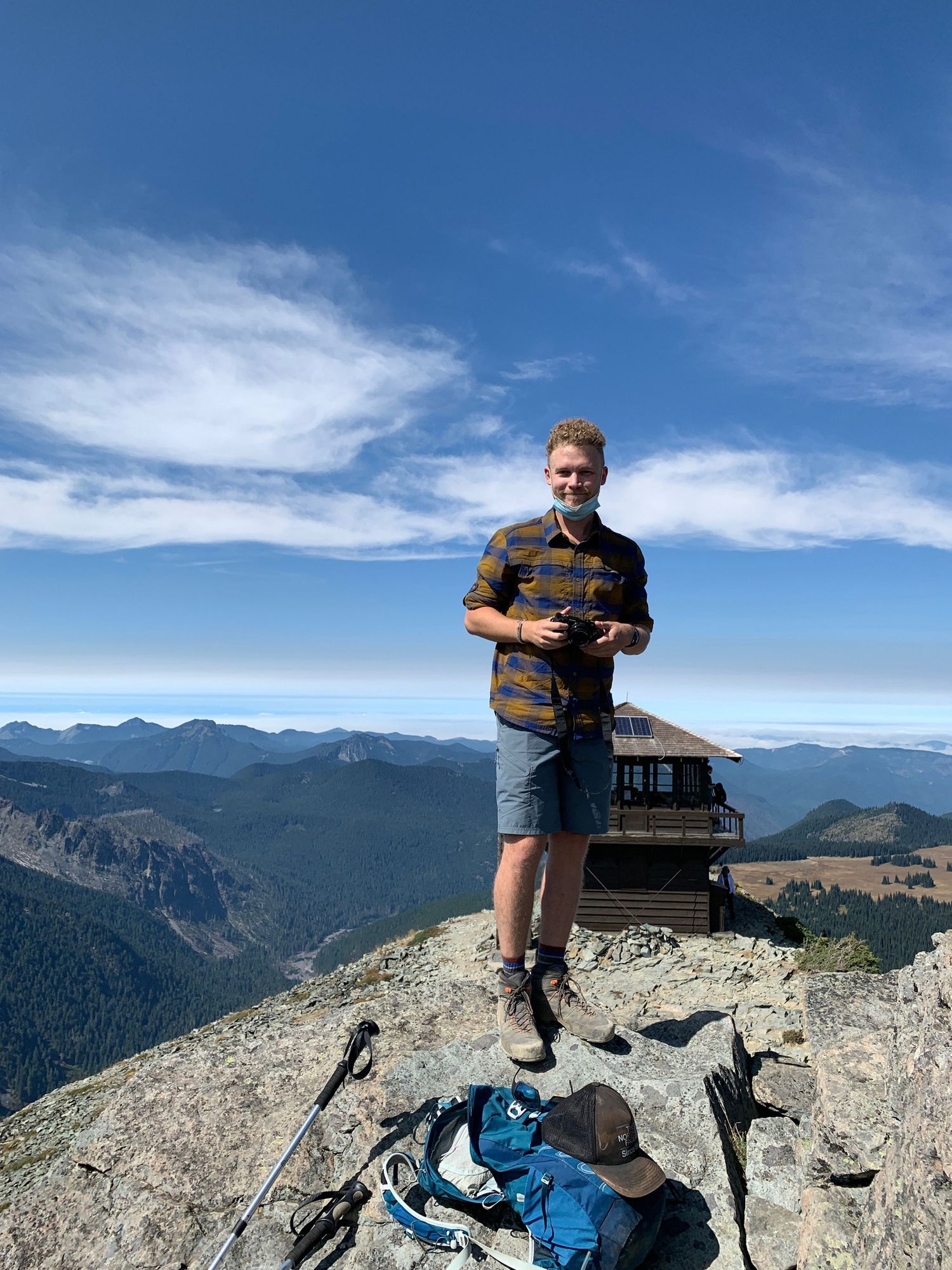 Hiker standing on a mountain summit with a fire lookout tower and scenic valley views behind.