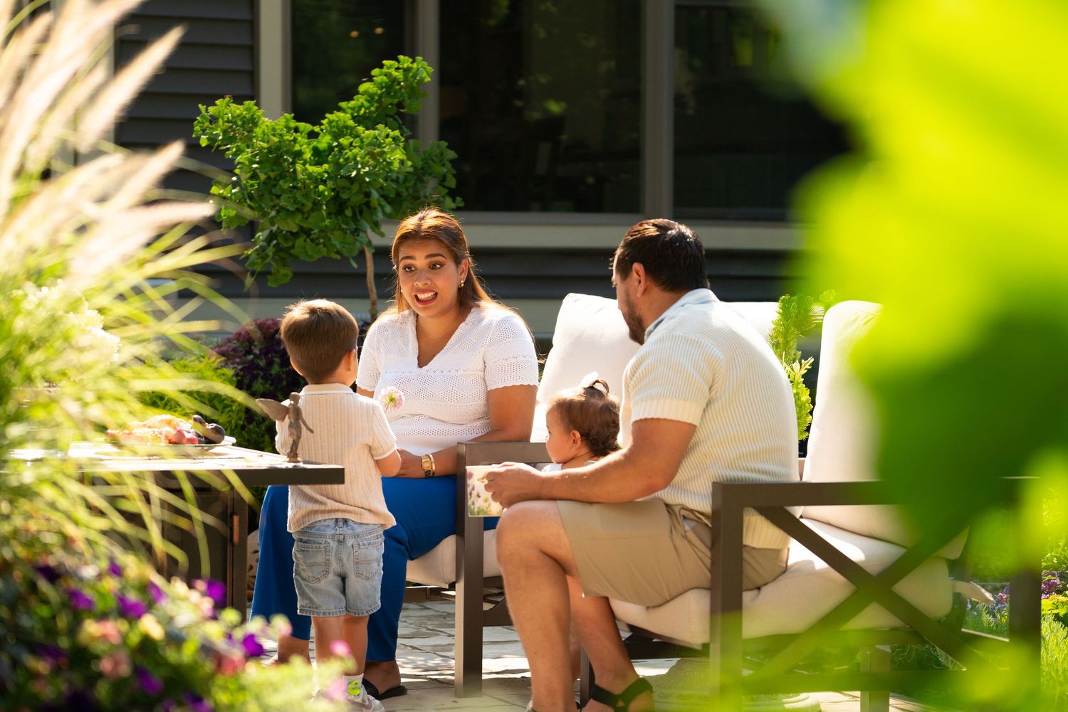 Family with two children relaxing on outdoor patio furniture surrounded by green plants.