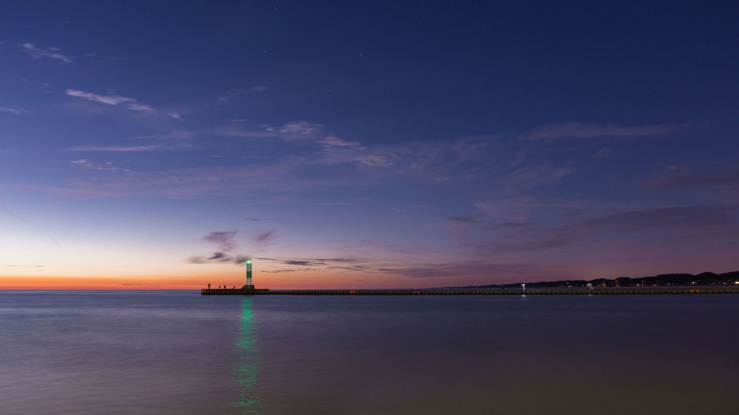 Serene twilight seascape with a distant lighthouse emitting green light over calm waters under a blue dusk sky.