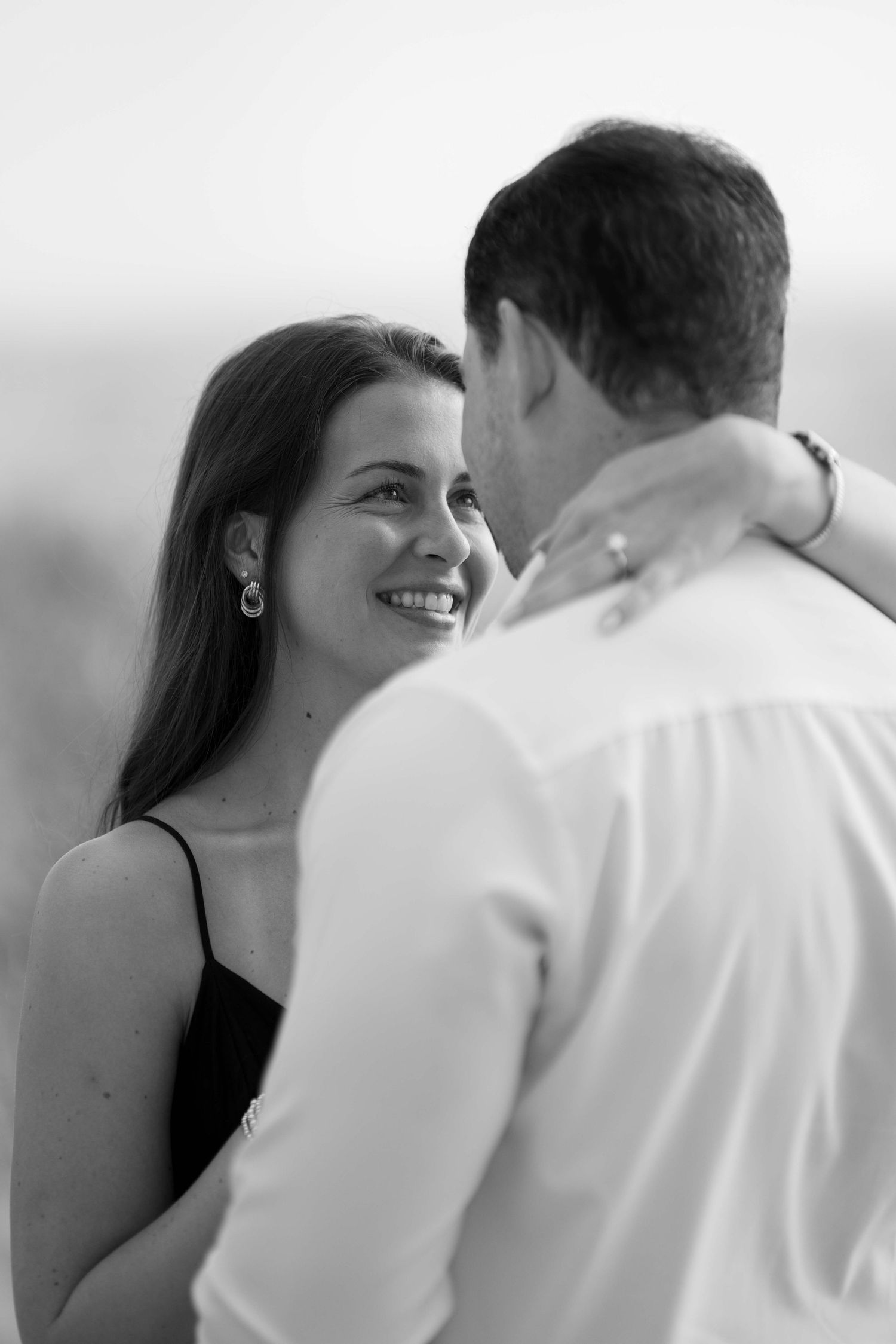 Black and white romantic photo of a smiling woman gazing up at her partner during an engagement session.