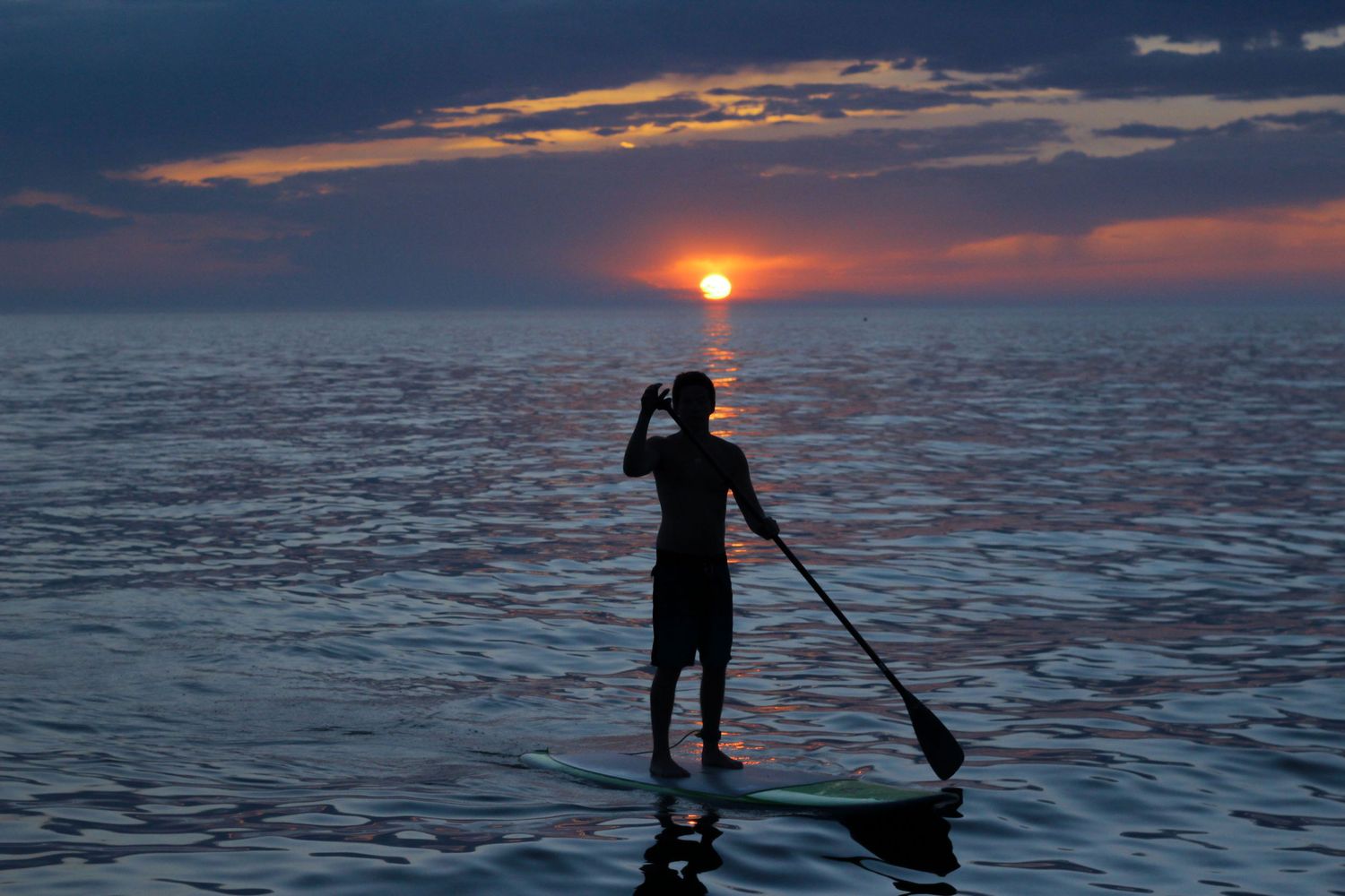 Silhouette of paddleboarder on calm ocean water at a vibrant colorful sunset.