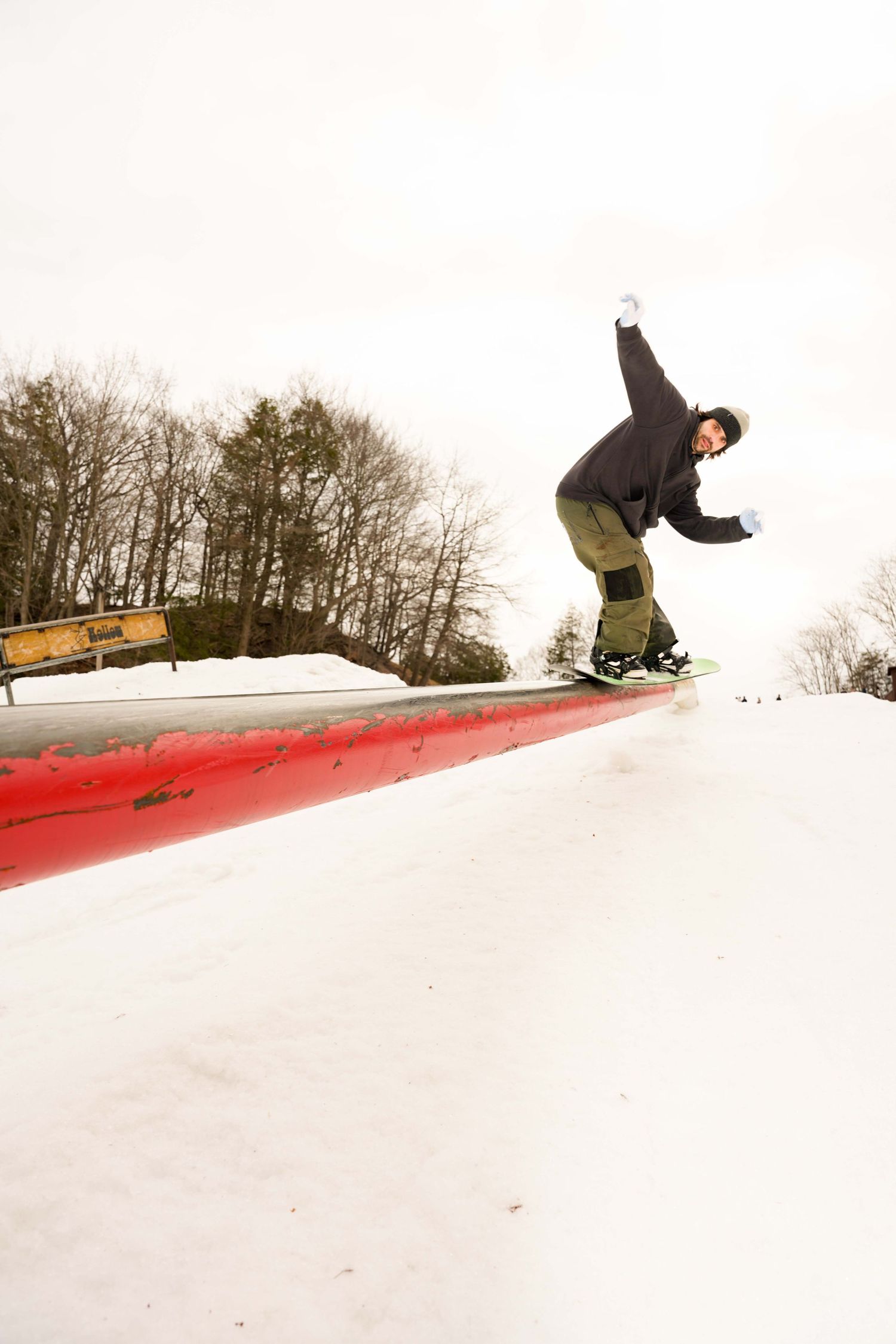 Snowboarder performing a grind trick on a red rail at a snow park in winter.
