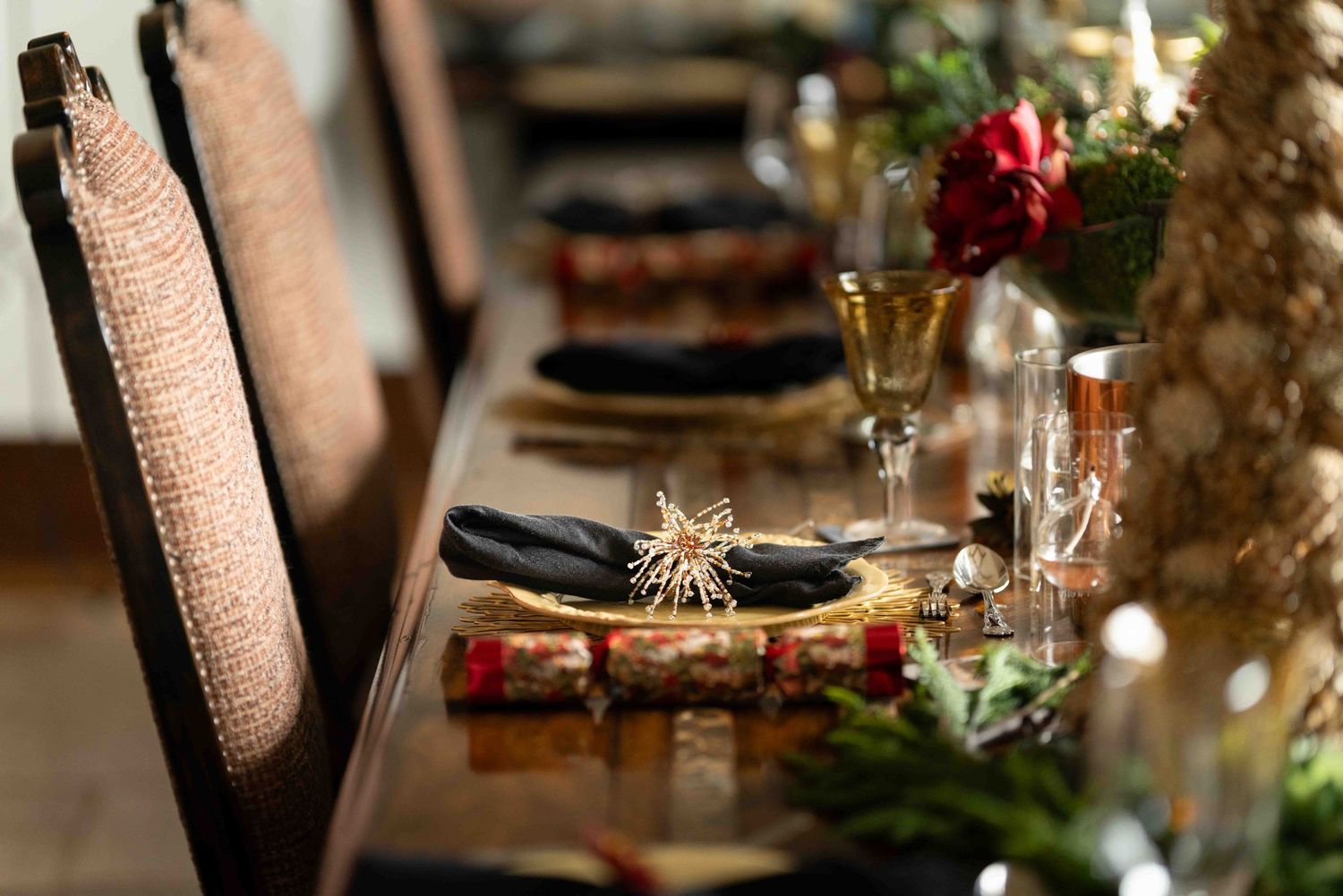 Elegant holiday dining table set with gold accents, black napkins, and red floral decor.