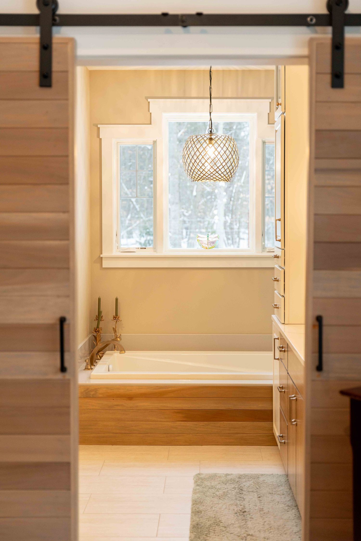 Warm bathroom with sliding barn door, wood-surround soaking tub, woven pendant light, and window.